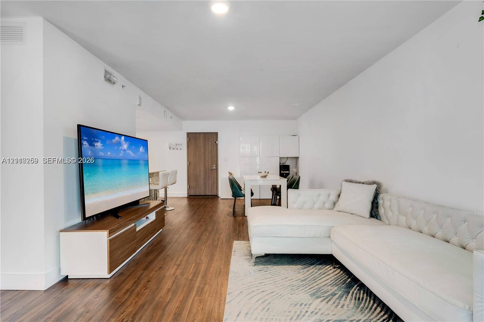 Open-concept living space featuring wood-finish flooring, recessed lighting, and high-gloss white built-in cabinetry