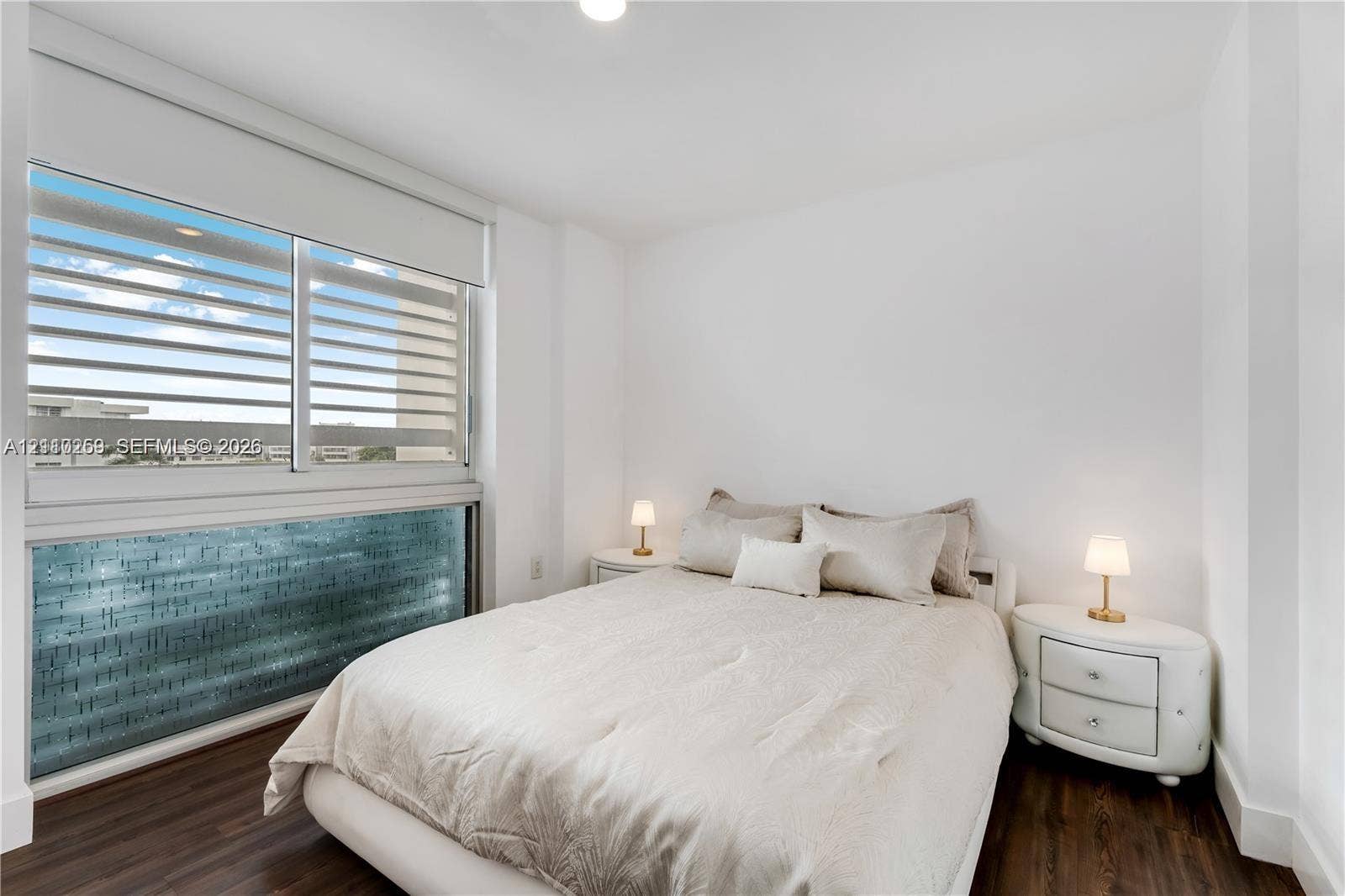 Room featuring dark wood-finish flooring, white walls, and a large horizontal window with integrated blinds