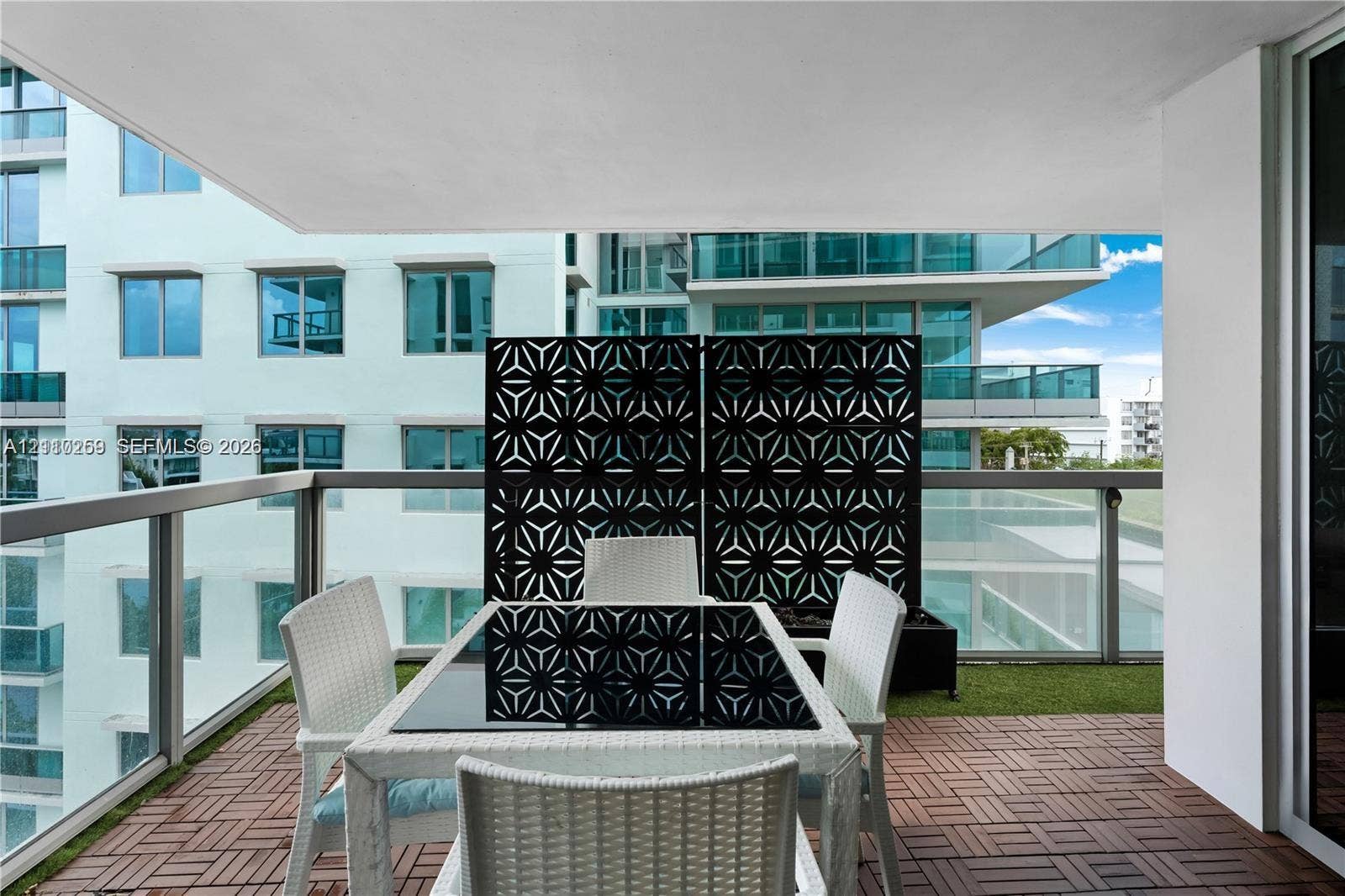 Covered balcony featuring interlocking deck tiles, glass paneled railings, and a decorative geometric privacy screen