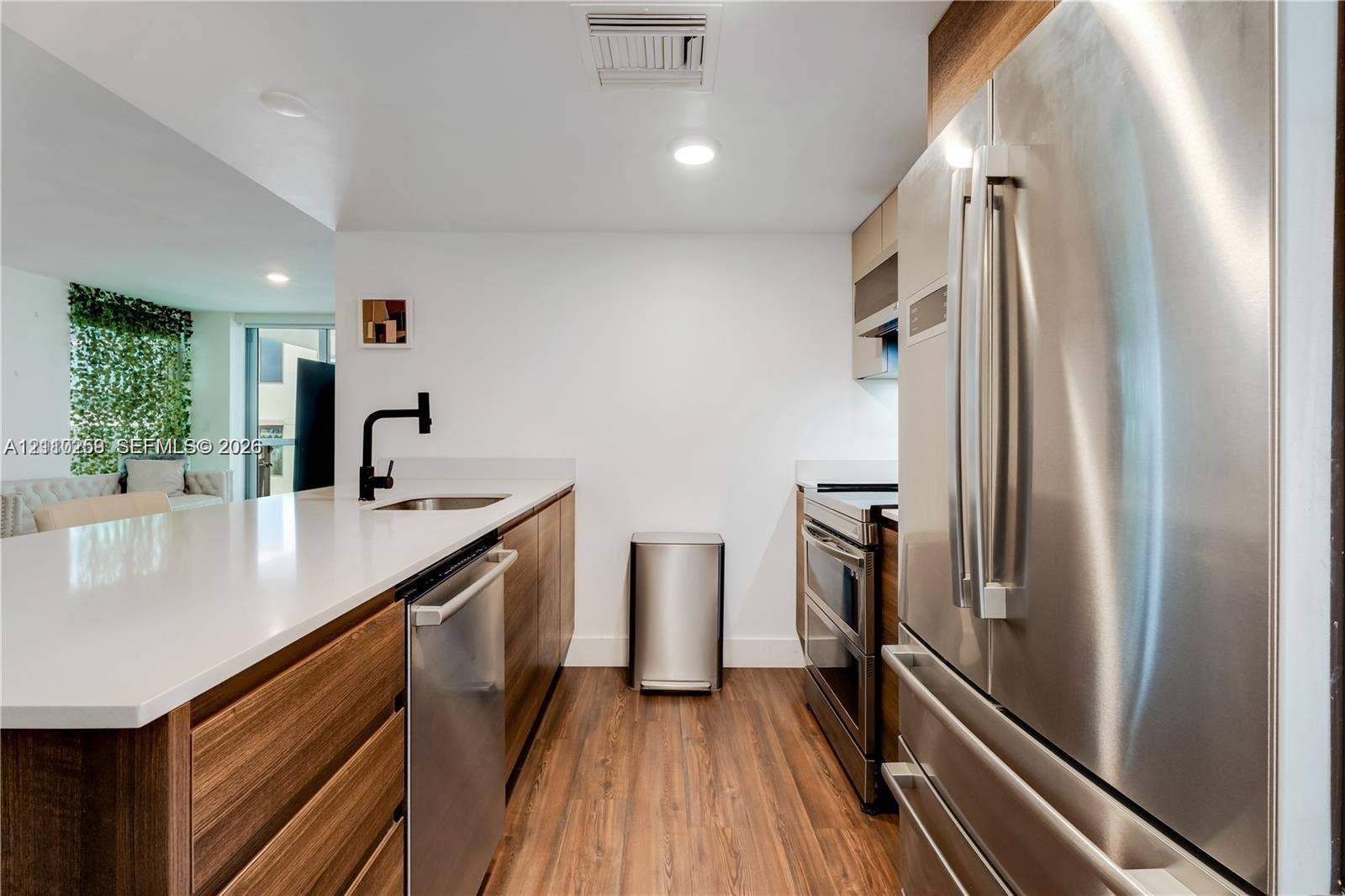 Kitchen featuring stainless steel appliances, wood-finish cabinetry, white solid-surface countertops, wood-finish flooring, and a matte black faucet
