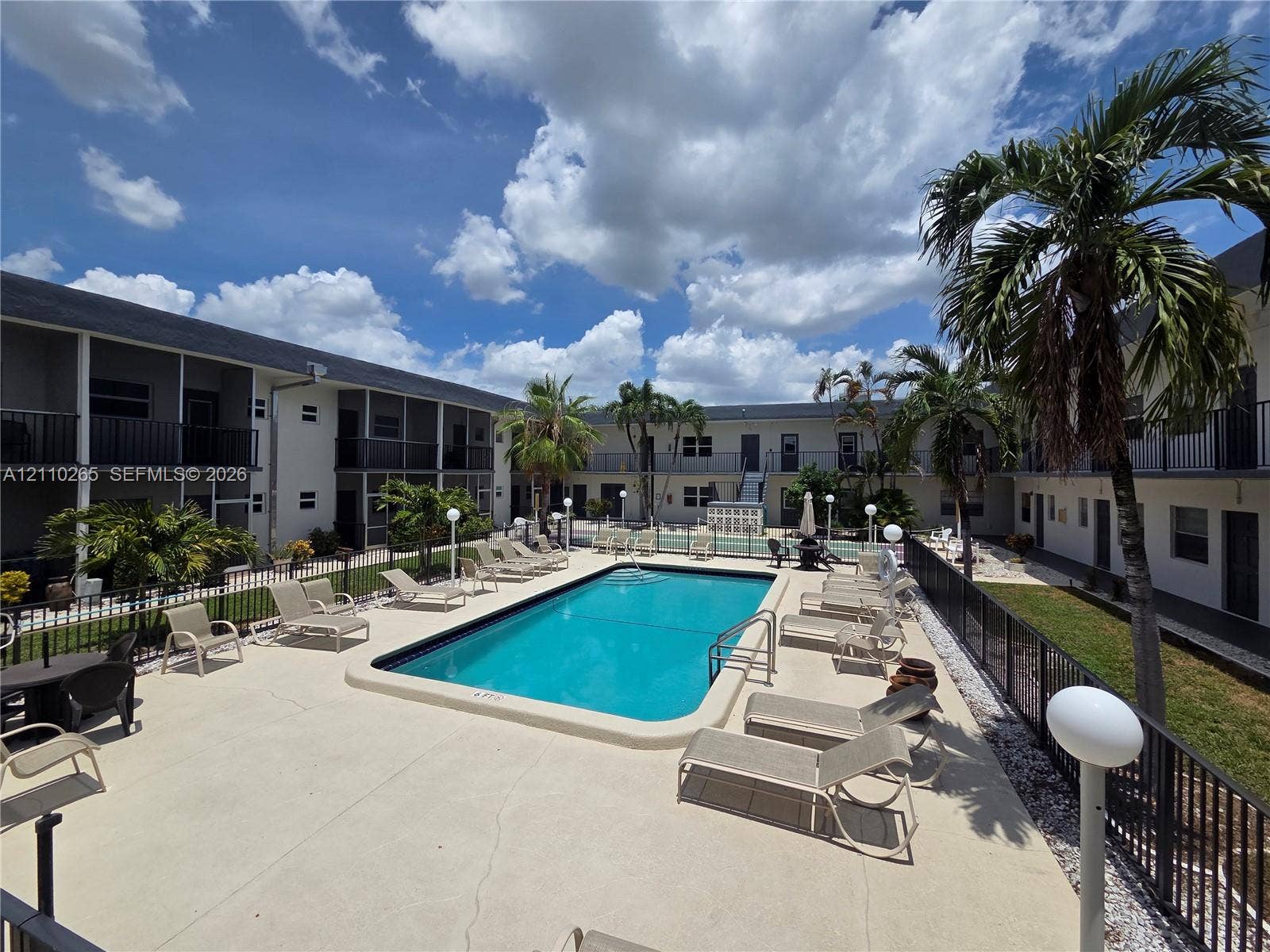 415 NE 2nd Street, #106, Hallandale Beach, Hallandale Beach, FL 33009 In-ground swimming pool featuring a concrete deck, metal perimeter fencing, and established palm trees