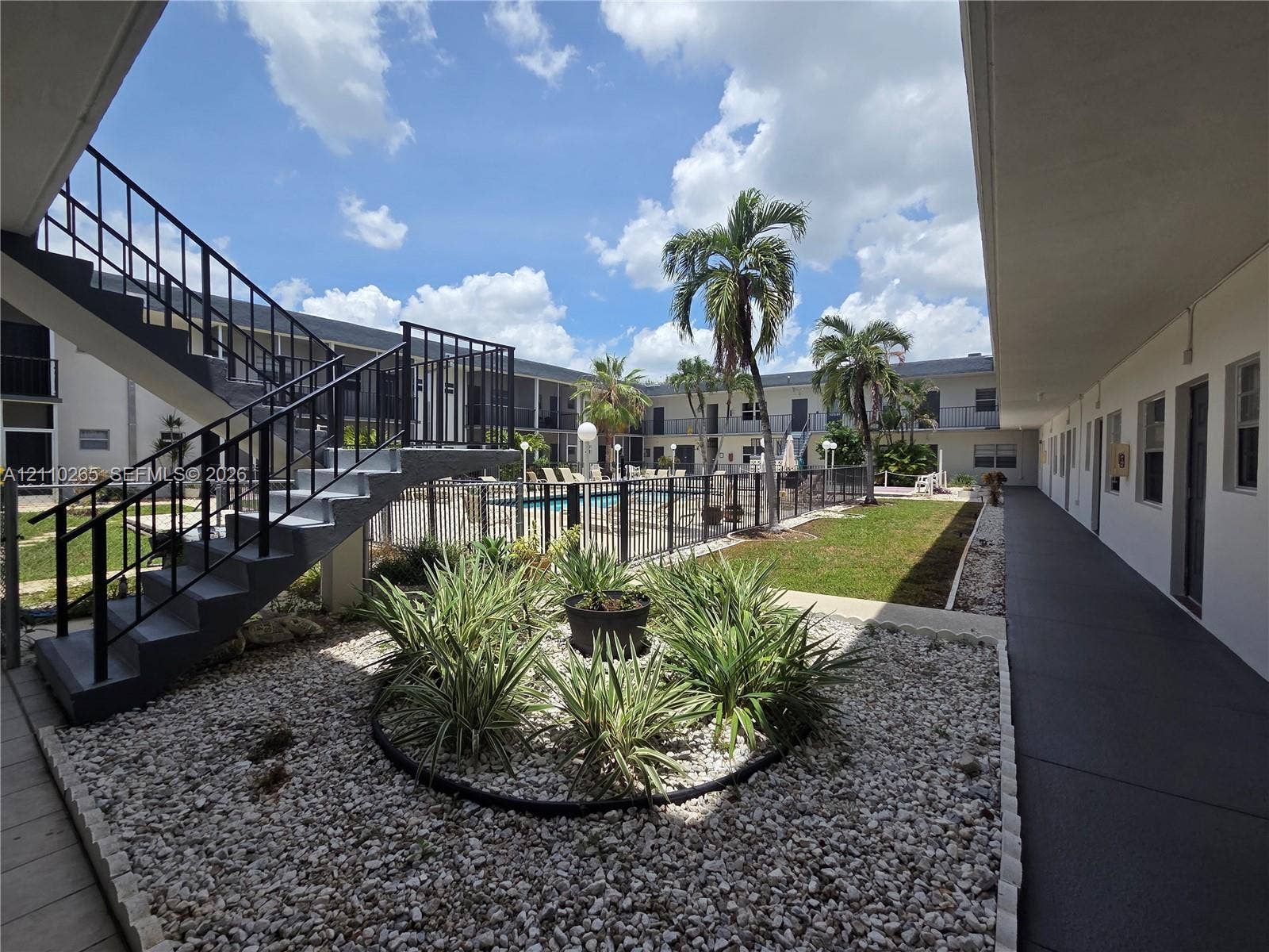 415 NE 2nd Street, #106, Hallandale Beach, Hallandale Beach, FL 33009 Courtyard featuring an outdoor swimming pool with metal perimeter fencing, landscaped rock gardens with native vegetation, palm trees, and metal staircases
