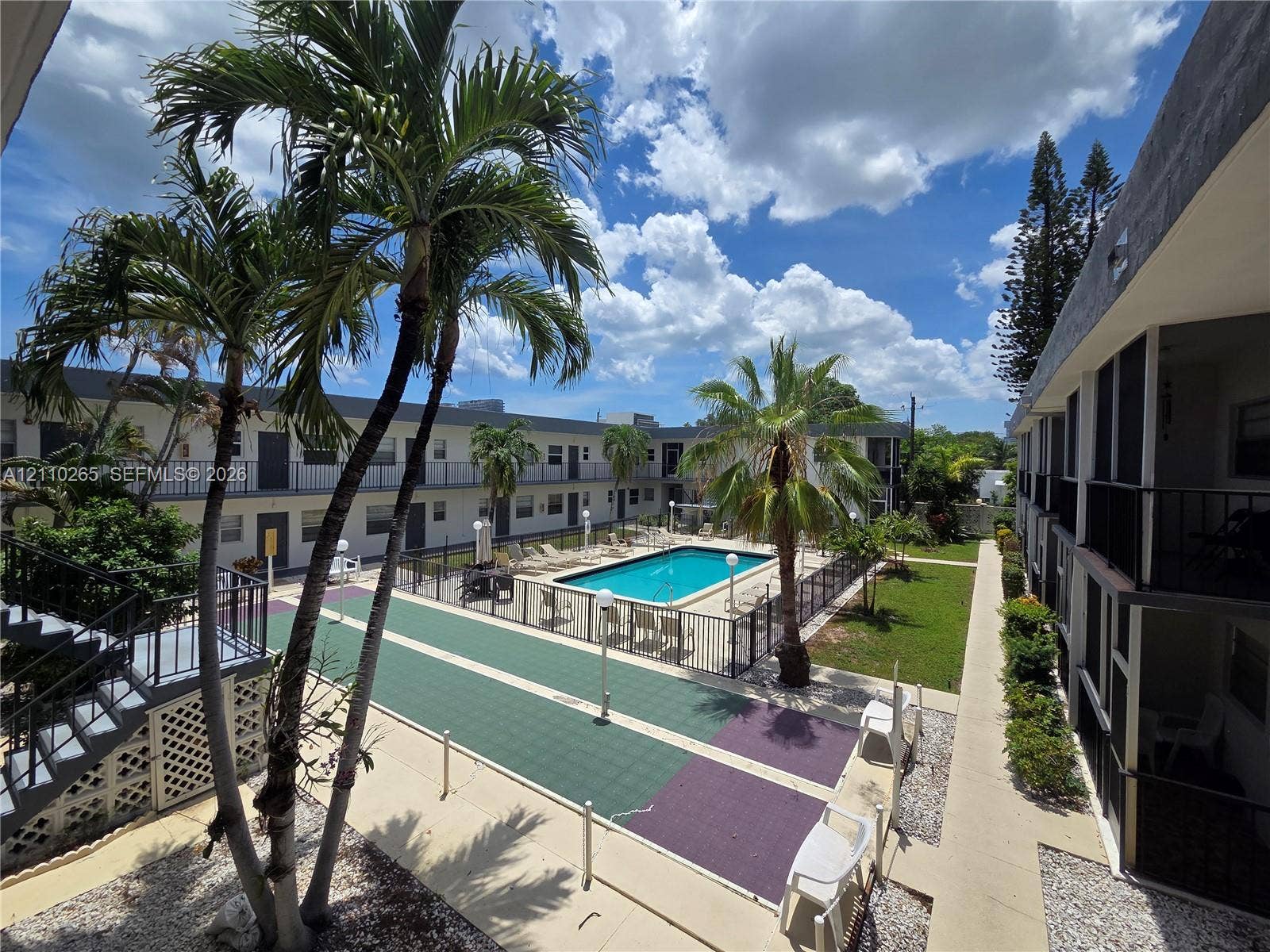 415 NE 2nd Street, #106, Hallandale Beach, Hallandale Beach, FL 33009 Swimming pool with security fencing, palm tree landscaping, paved recreation area, and multi-story building exterior