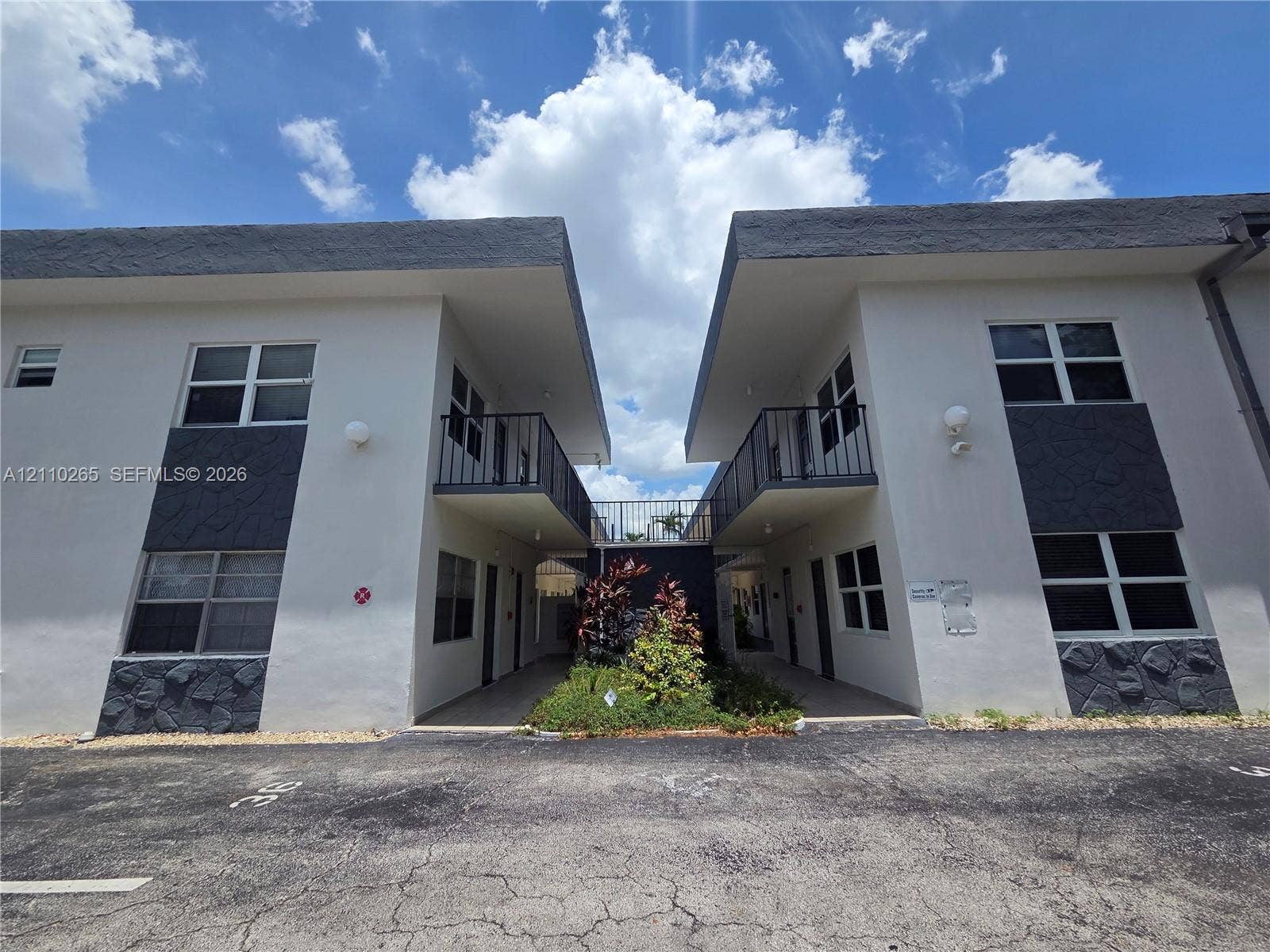 415 NE 2nd Street, #106, Hallandale Beach, Hallandale Beach, FL 33009 Two-story exterior featuring white stucco facades, dark stone veneer accents, flat rooflines, and metal balcony railings
