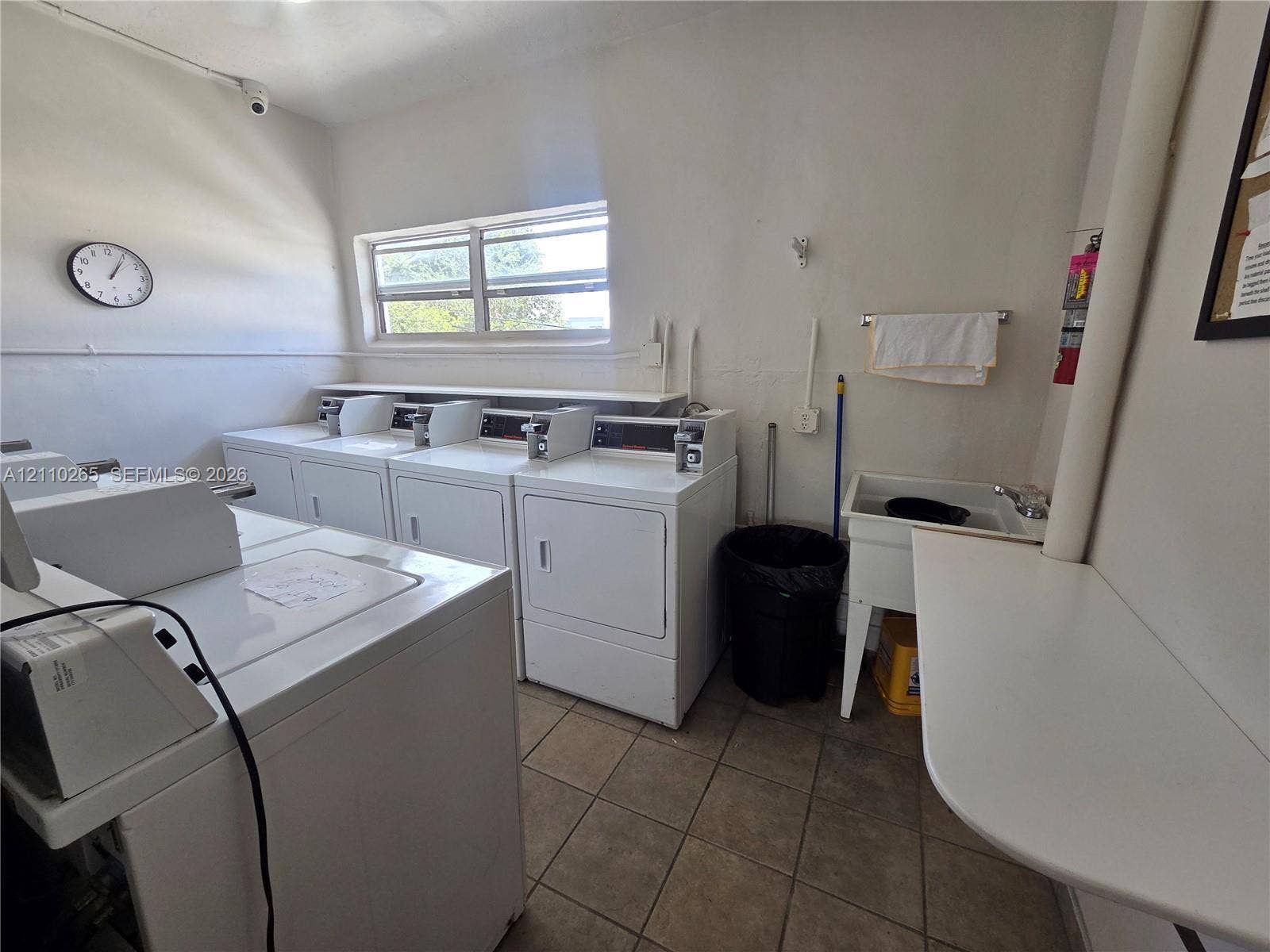 415 NE 2nd Street, #106, Hallandale Beach, Hallandale Beach, FL 33009 Laundry room featuring tile flooring, multiple washing and drying units, a built-in utility sink, and a wall-mounted folding counter