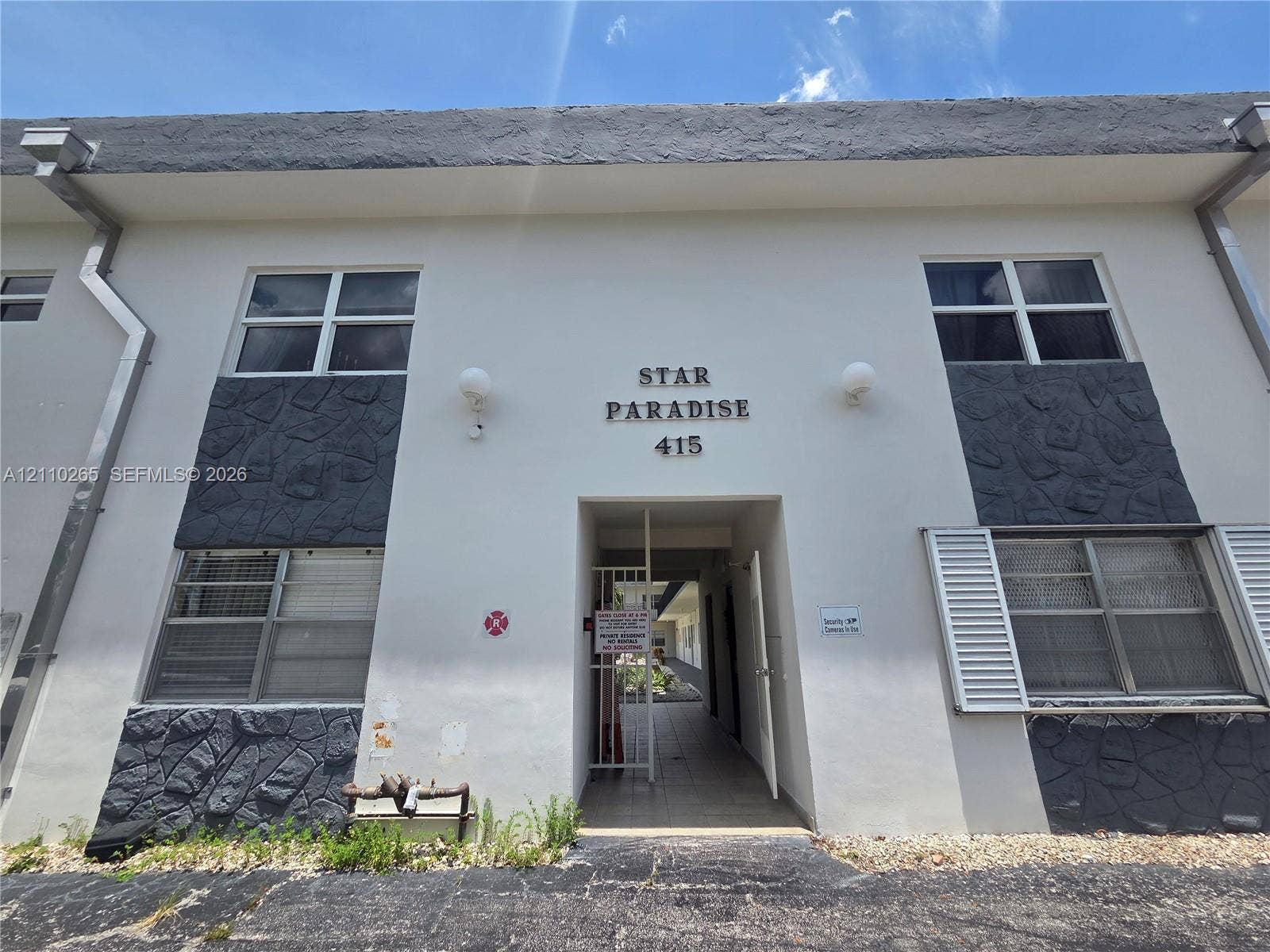 415 NE 2nd Street, #106, Hallandale Beach, Hallandale Beach, FL 33009 Stucco exterior facade featuring stone-veneer accents, multi-pane windows with louvered shutters, and dual wall-mounted exterior light fixtures