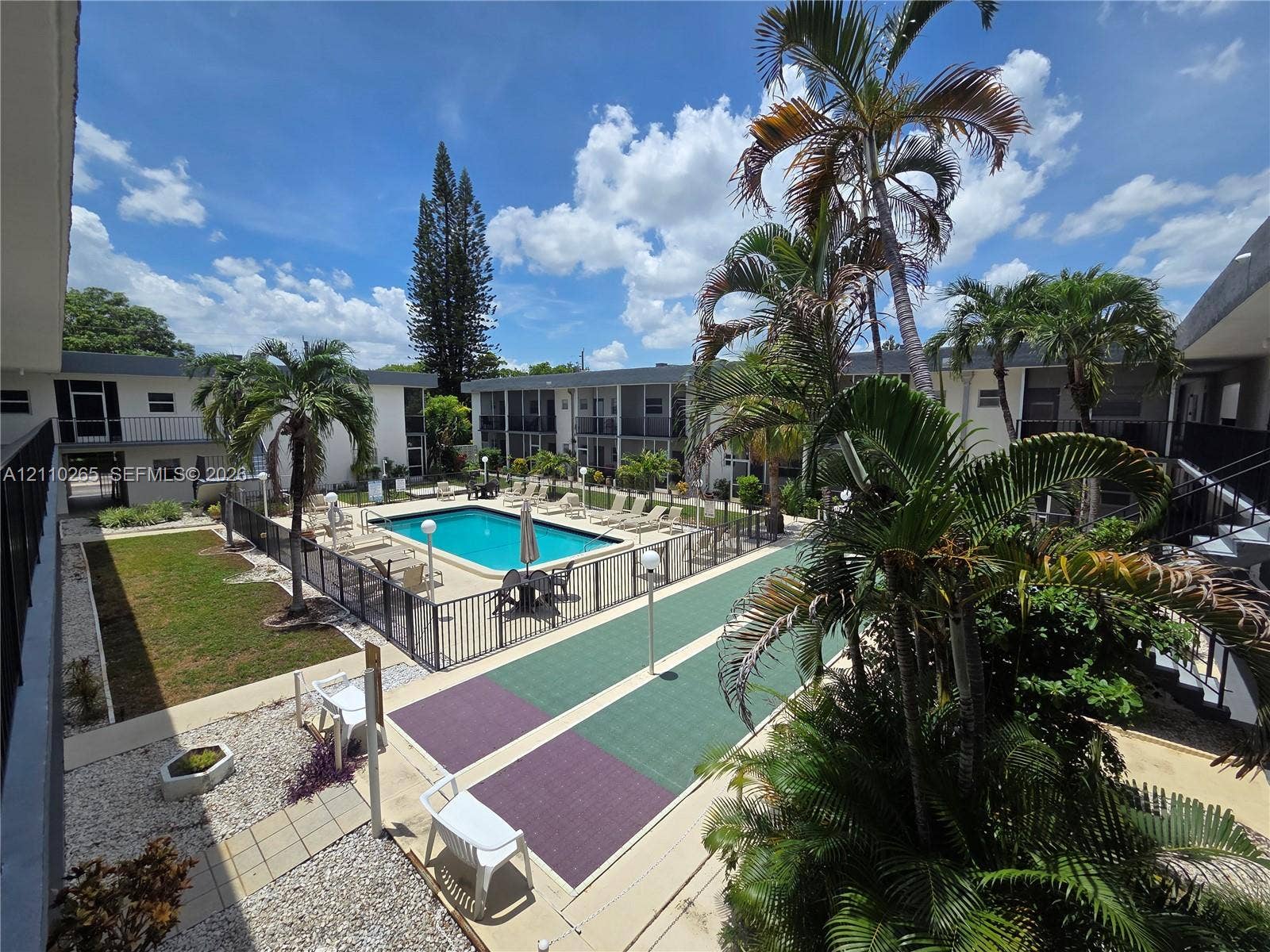415 NE 2nd Street, #106, Hallandale Beach, Hallandale Beach, FL 33009 Outdoor recreation area featuring an in-ground swimming pool, perimeter metal fencing, a hard-surface game court, and mature palm trees