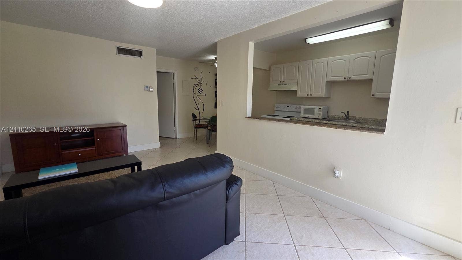 415 NE 2nd Street, #106, Hallandale Beach, Hallandale Beach, FL 33009 Open-concept interior featuring light-colored tile flooring, a kitchen pass-through, white shaker-style cabinetry, and a stone-finish countertop