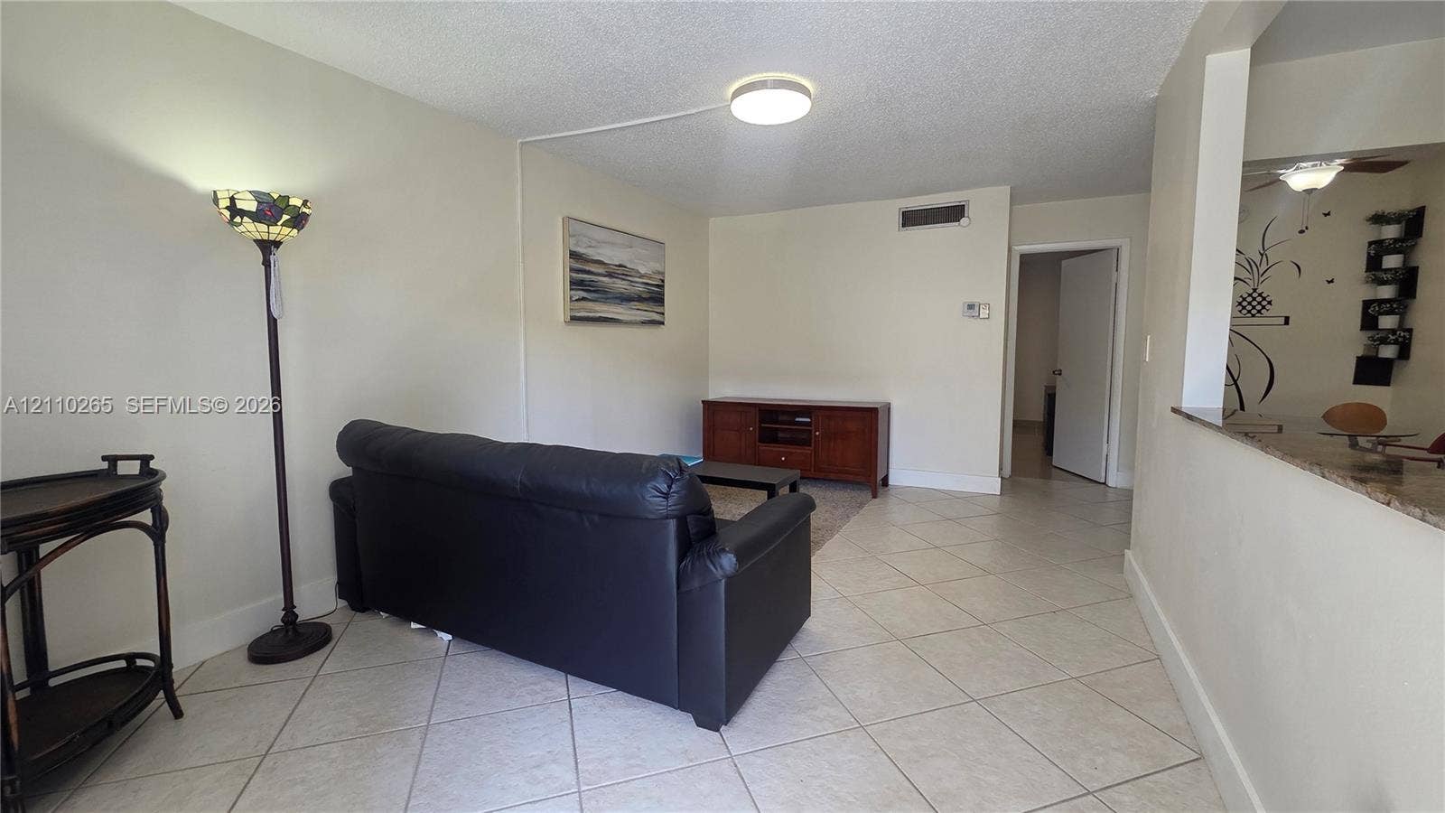 415 NE 2nd Street, #106, Hallandale Beach, Hallandale Beach, FL 33009 Neutral-toned interior space featuring diagonal tile flooring, a flush-mount ceiling light fixture, and a pass-through opening with stone-finish countertop