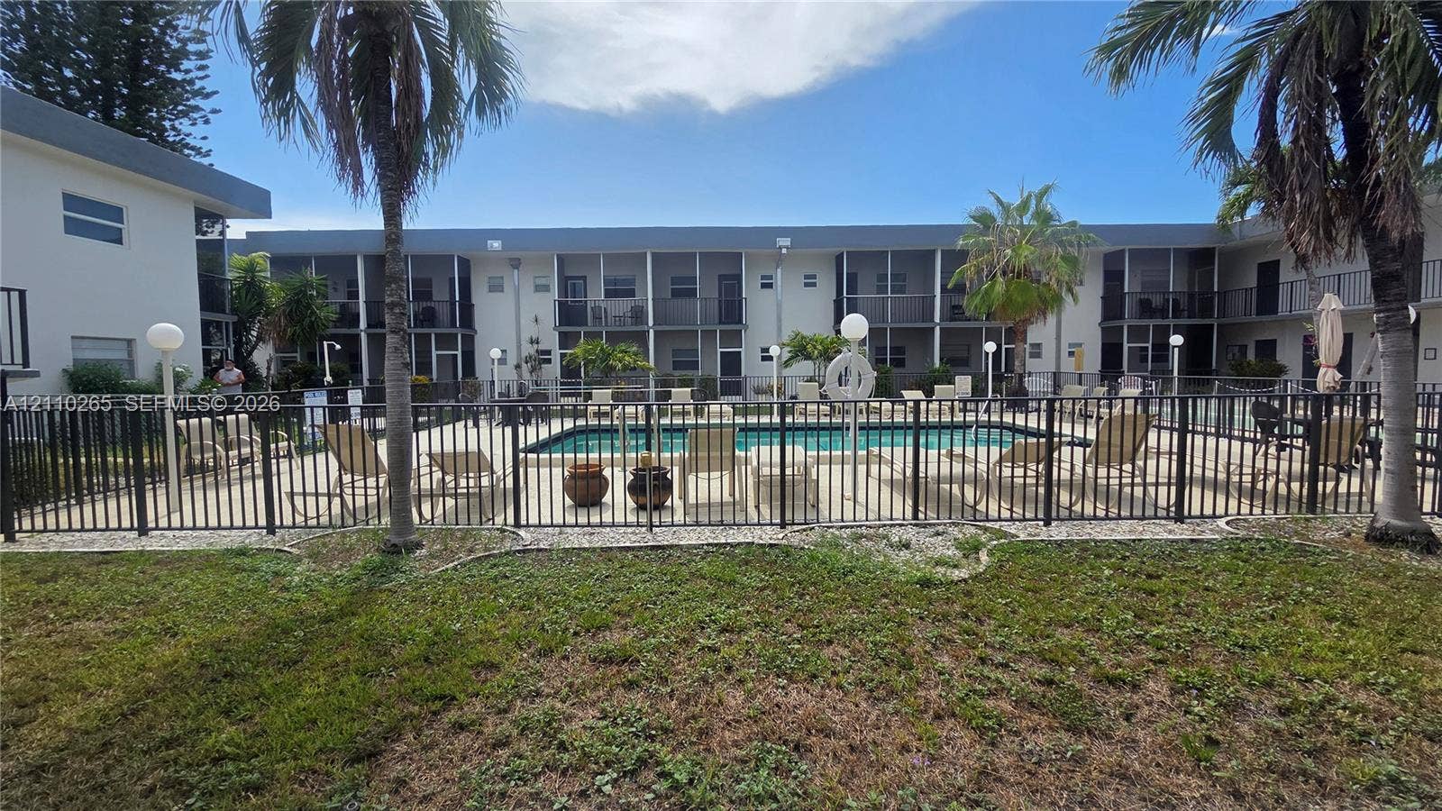 415 NE 2nd Street, #106, Hallandale Beach, Hallandale Beach, FL 33009 Swimming pool area featuring a metal security fence, paved perimeter, and mature palm trees