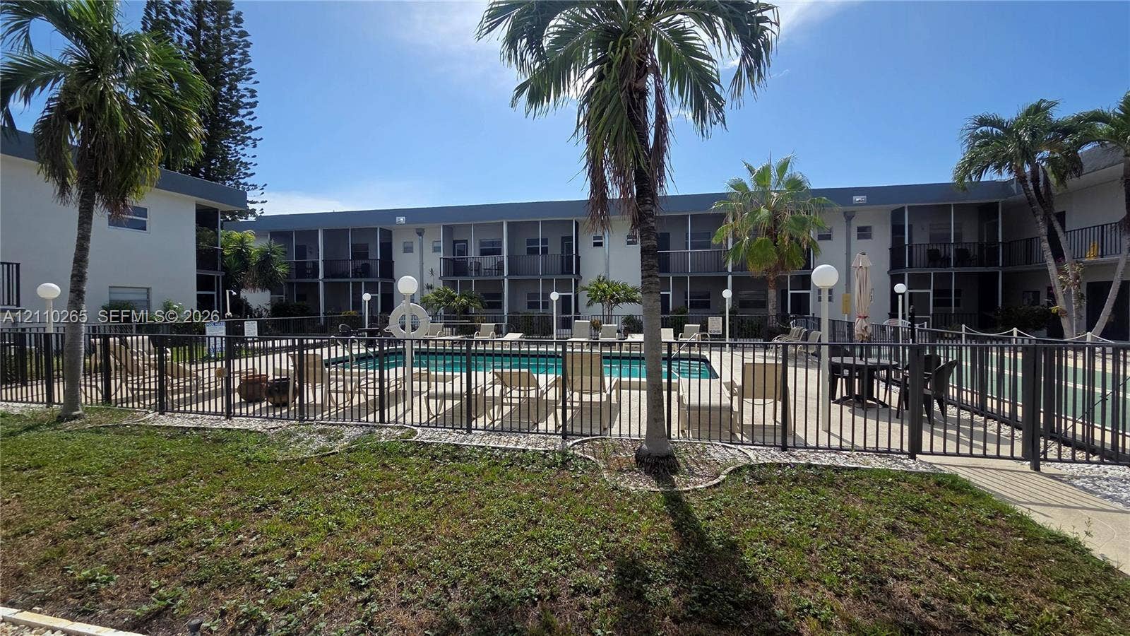 415 NE 2nd Street, #106, Hallandale Beach, Hallandale Beach, FL 33009 Swimming pool with a paved deck, perimeter metal fencing, and surrounding palm trees