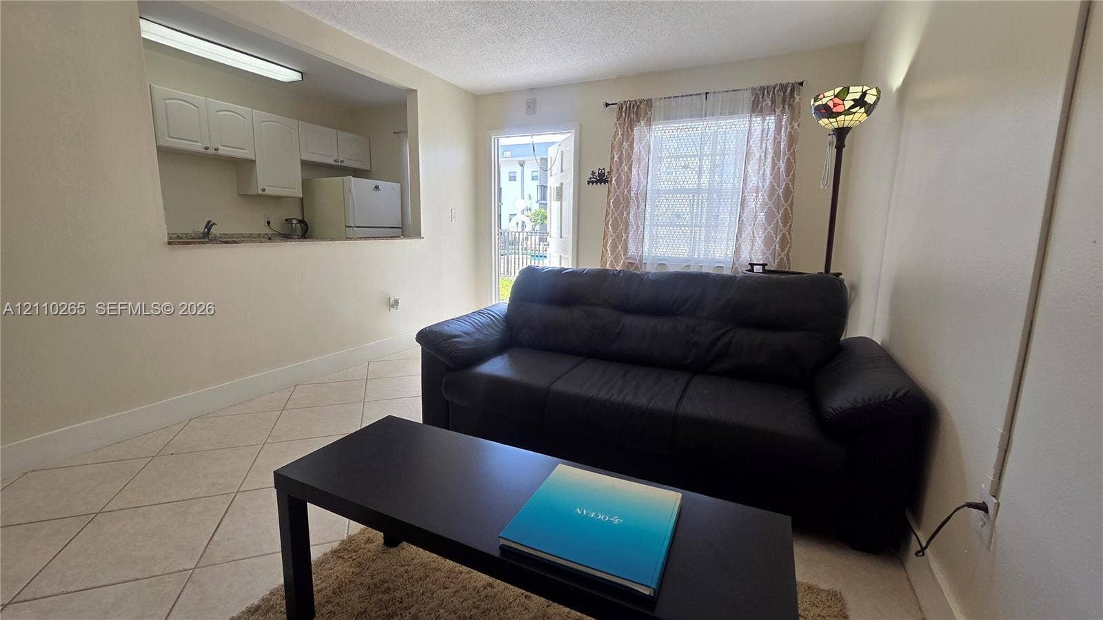 415 NE 2nd Street, #106, Hallandale Beach, Hallandale Beach, FL 33009 Open-concept interior featuring neutral wall tones, ceramic tile flooring set on the diagonal, and a kitchen pass-through window with built-in cabinetry