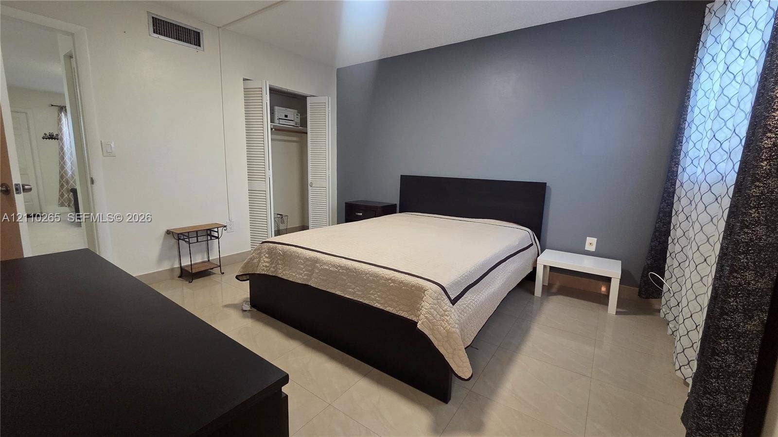 415 NE 2nd Street, #106, Hallandale Beach, Hallandale Beach, FL 33009 Room featuring neutral large-format tile flooring, a charcoal gray accent wall, and a double-door closet with louvered panels