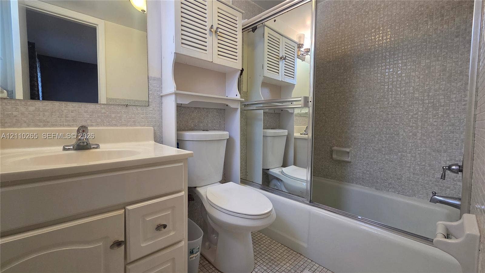 415 NE 2nd Street, #106, Hallandale Beach, Hallandale Beach, FL 33009 Bathroom featuring a vanity with integrated sink, built-in over-the-toilet storage cabinetry, mirrored sliding shower enclosure, and mosaic-tiled shower surround