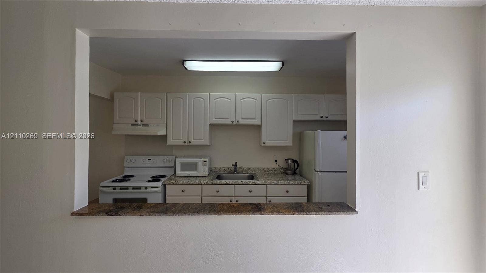 415 NE 2nd Street, #106, Hallandale Beach, Hallandale Beach, FL 33009 Kitchen featuring white cabinetry, stone-finish countertops, stainless steel sink, and built-in pass-through counter