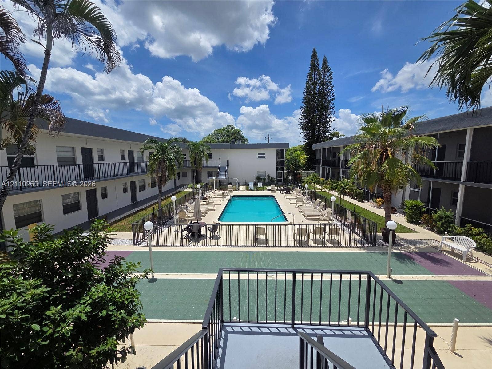 415 NE 2nd Street, #106, Hallandale Beach, Hallandale Beach, FL 33009 Courtyard featuring an in-ground swimming pool, fenced pool deck, paved recreational space, and mature palm trees
