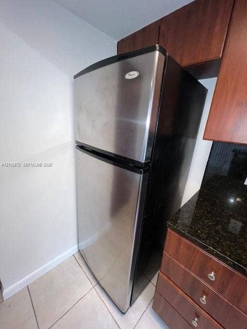 Stainless steel top-freezer refrigerator, dark wood-finish cabinetry, and stone-surface countertop