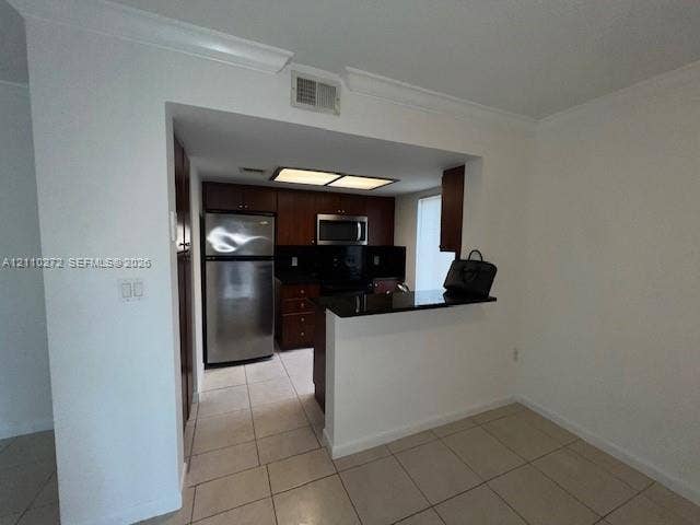 Kitchen featuring dark wood cabinetry, stainless steel appliances, black countertops, and tile flooring