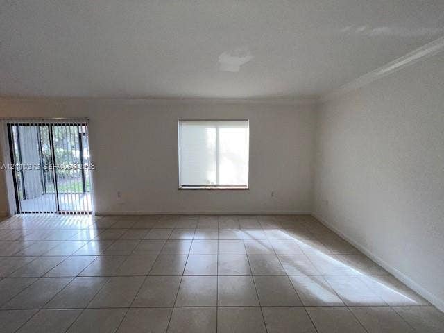 Large-format tile flooring, neutral wall tones, crown molding, double-pane window, and sliding glass door