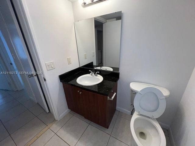 Vanity featuring a dark stone countertop, integrated sink, wood-finish cabinetry, a full-height wall mirror, and tile flooring