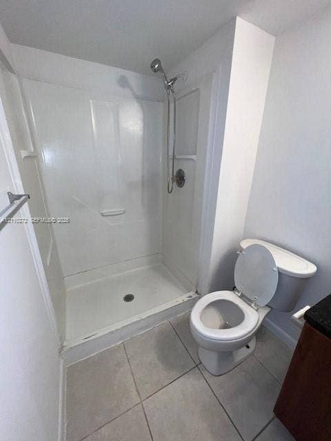Full-height shower enclosure with a handheld showerhead, two-piece toilet, and tile flooring