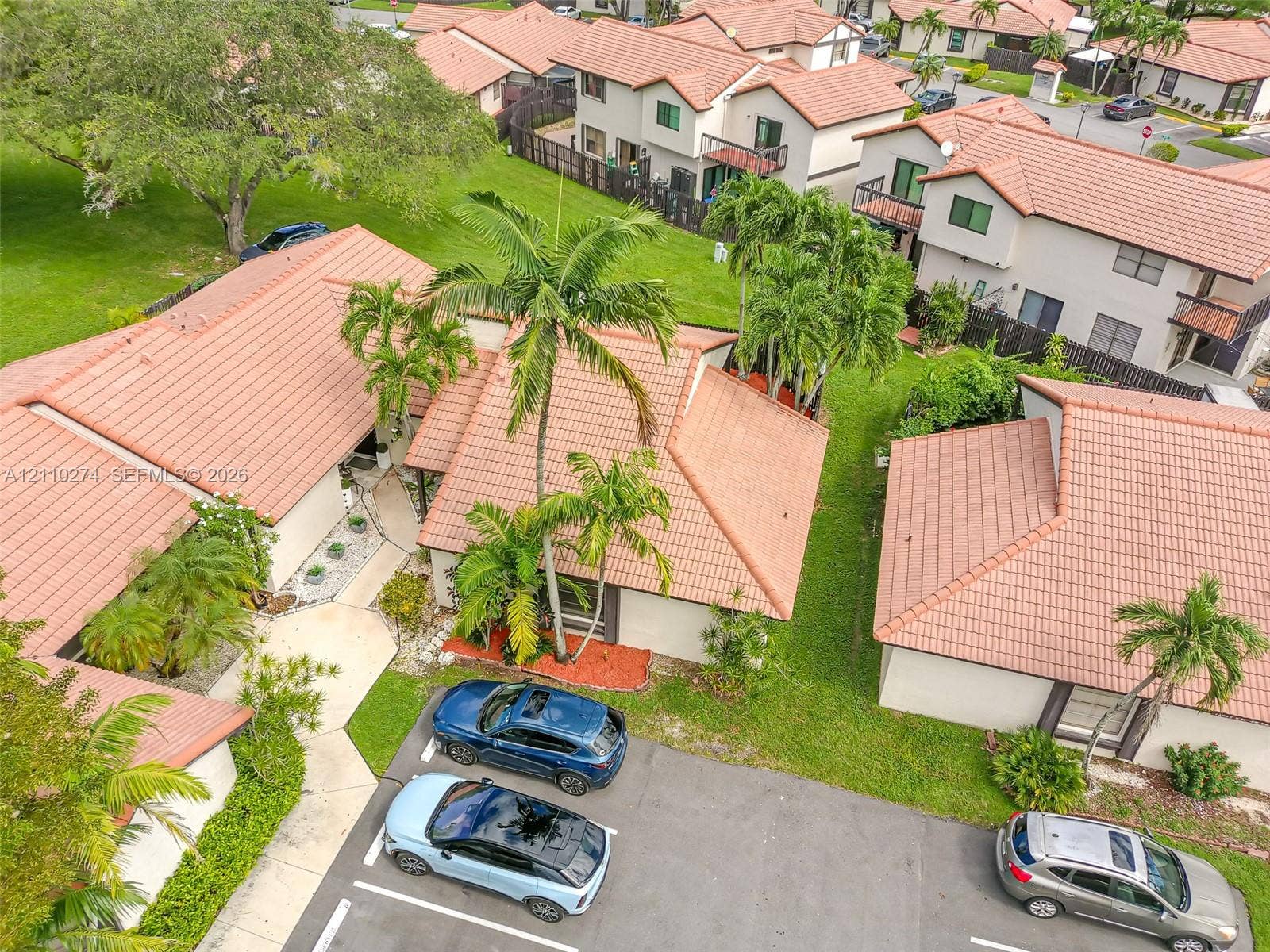 14955 SW 49th Lane, #5E, Miami, FL 33185 Aerial view featuring terracotta-style roof tiles, mature palm trees, designated parking spaces, and landscaped exterior grounds