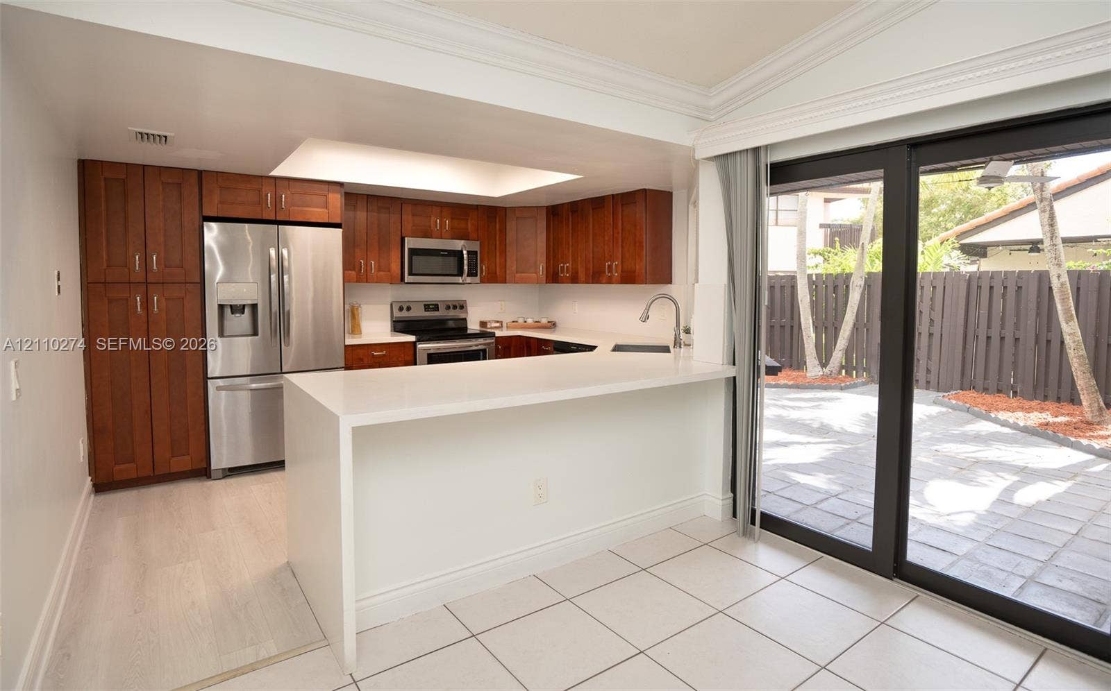 14955 SW 49th Lane, #5E, Miami, FL 33185 Kitchen featuring wood cabinetry, stainless steel appliances, white quartz countertops with a waterfall edge, recessed lighting, and sliding glass doors opening to a paved patio