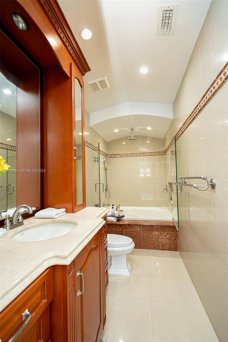 14955 SW 49th Lane, #5E, Miami, FL 33185 Bathroom featuring a wood-finish vanity with a stone countertop, an integrated jetted tub with stone tile surround, a glass-enclosed shower, and polished tile flooring