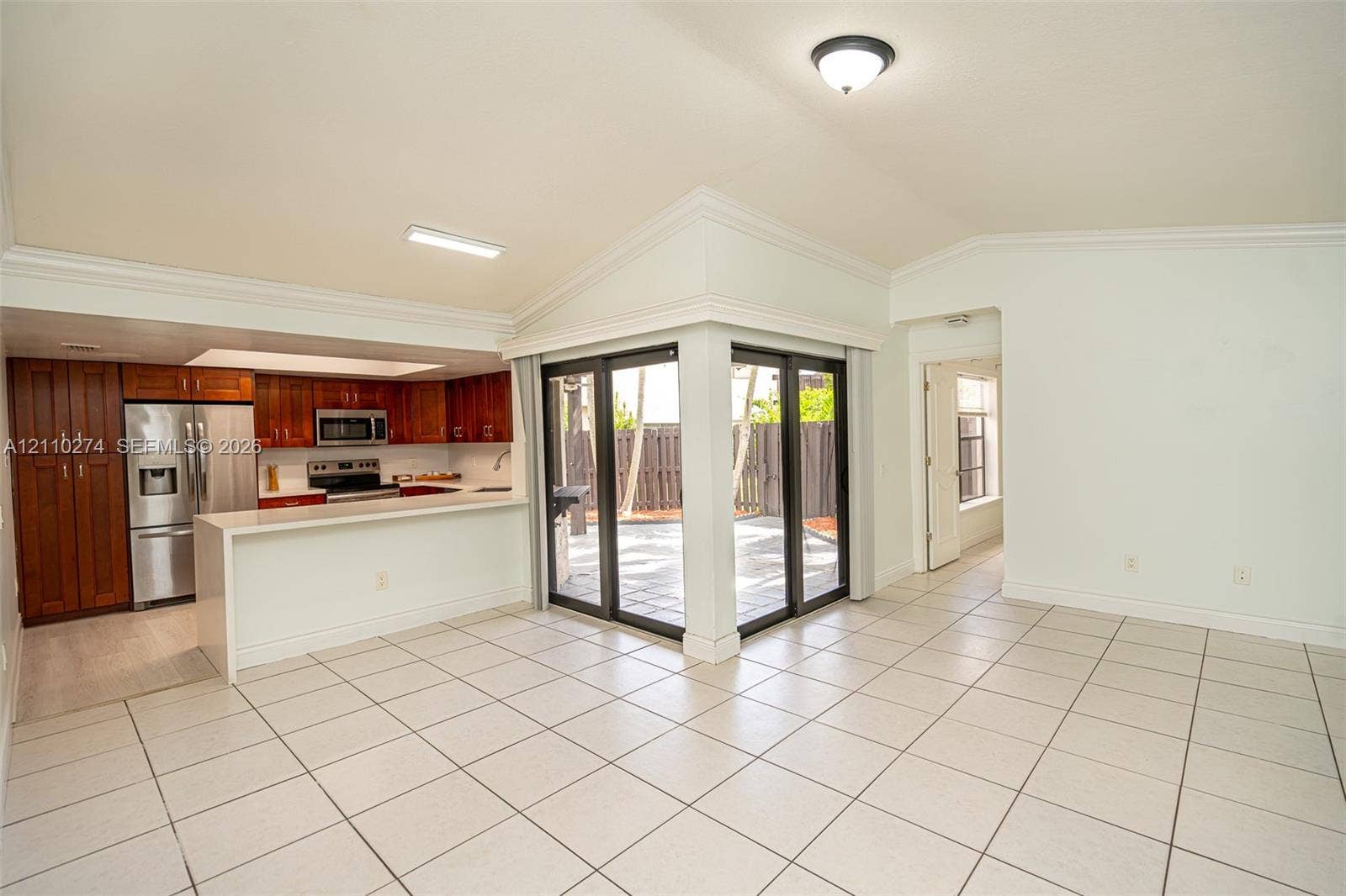 14955 SW 49th Lane, #5E, Miami, FL 33185 Kitchen featuring wood cabinetry, stainless steel appliances, and a breakfast bar, with vaulted ceilings and sliding glass doors opening to a paved exterior space