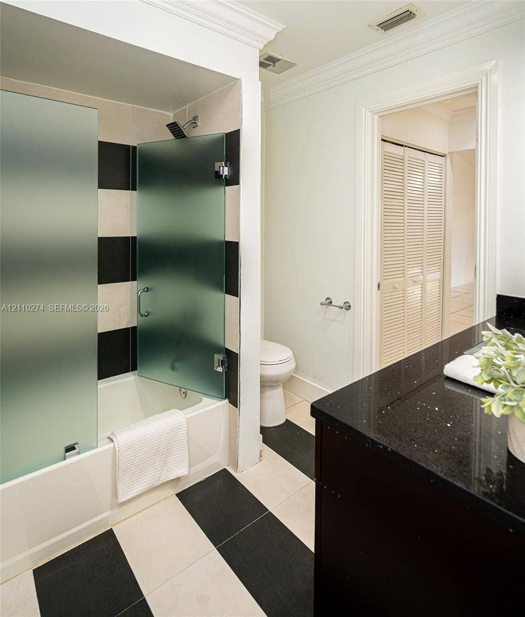 14955 SW 49th Lane, #5E, Miami, FL 33185 Bathroom featuring a vanity with a dark stone countertop, bathtub with a frosted glass enclosure, and a black-and-white tiled floor