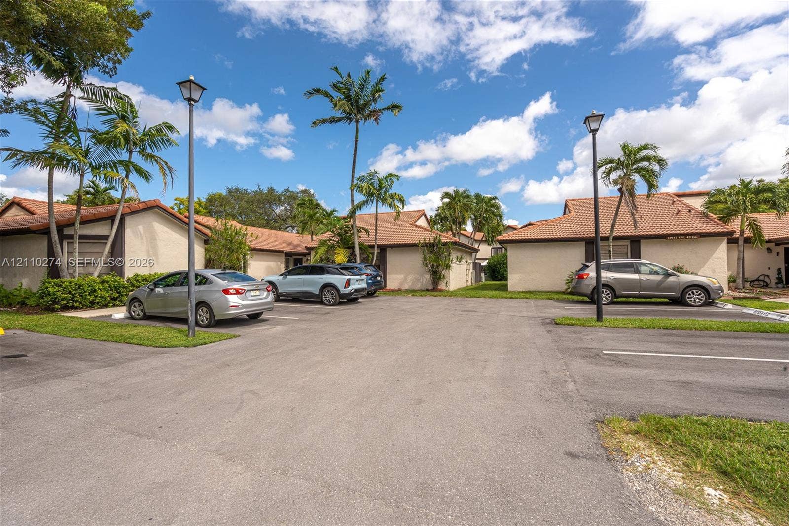 14955 SW 49th Lane, #5E, Miami, FL 33185 Single-story building exteriors featuring stucco facades, multi-pitched tile roofing, dedicated surface parking, and mature palm landscaping with integrated pole lighting