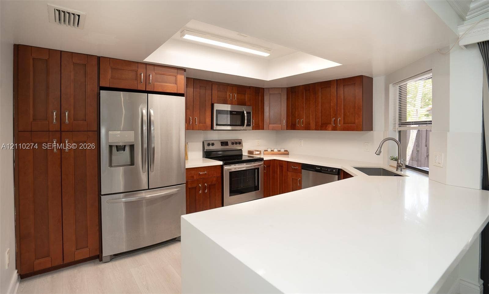 14955 SW 49th Lane, #5E, Miami, FL 33185 Kitchen featuring warm-toned wood cabinetry, stainless steel appliances, solid surface countertops, a recessed ceiling fixture, and a single-basin undermount sink