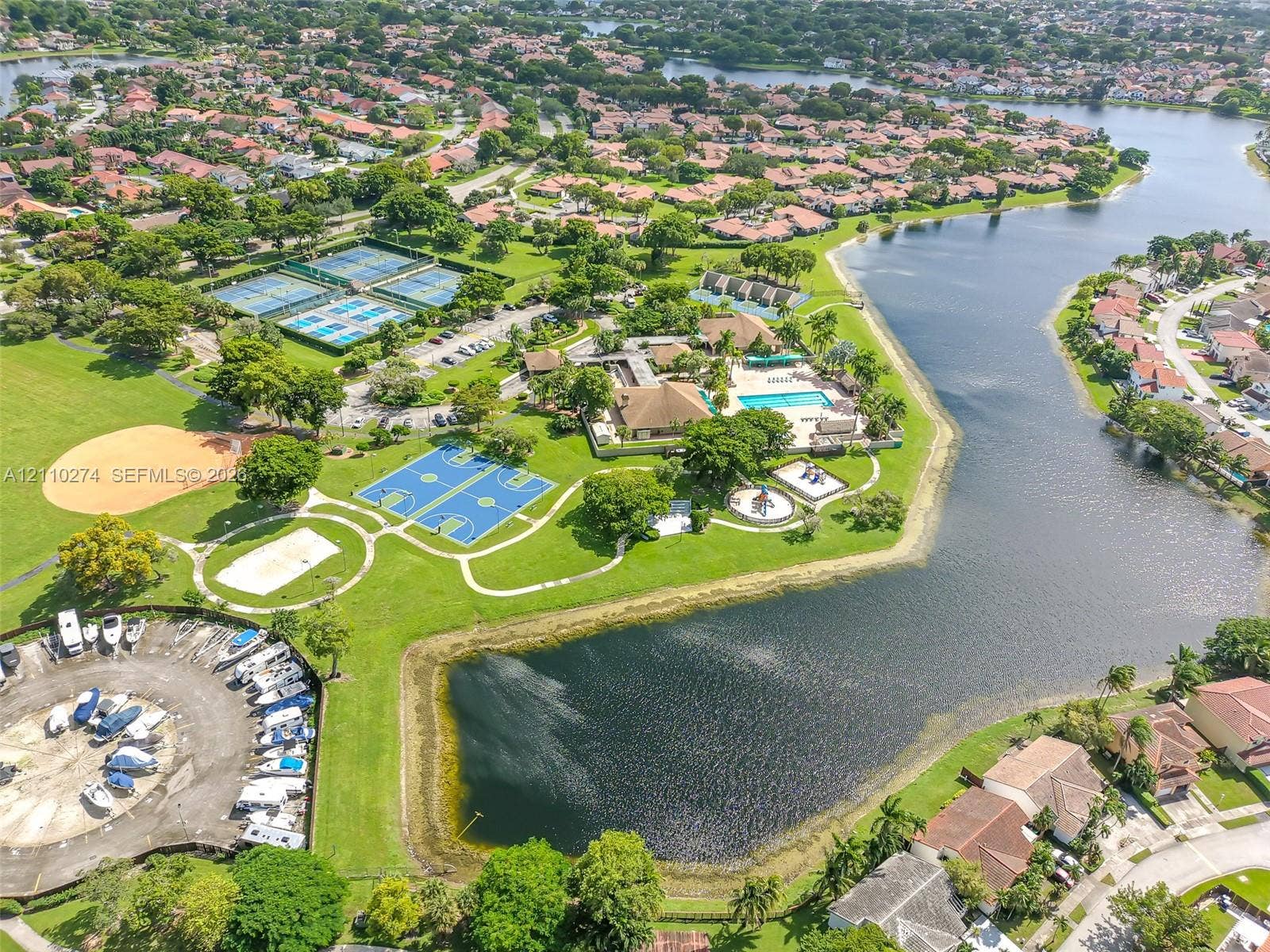 14955 SW 49th Lane, #5E, Miami, FL 33185 Aerial perspective of community grounds featuring a swimming pool, tennis courts, basketball court, baseball diamond, and boat storage area situated alongside a lake
