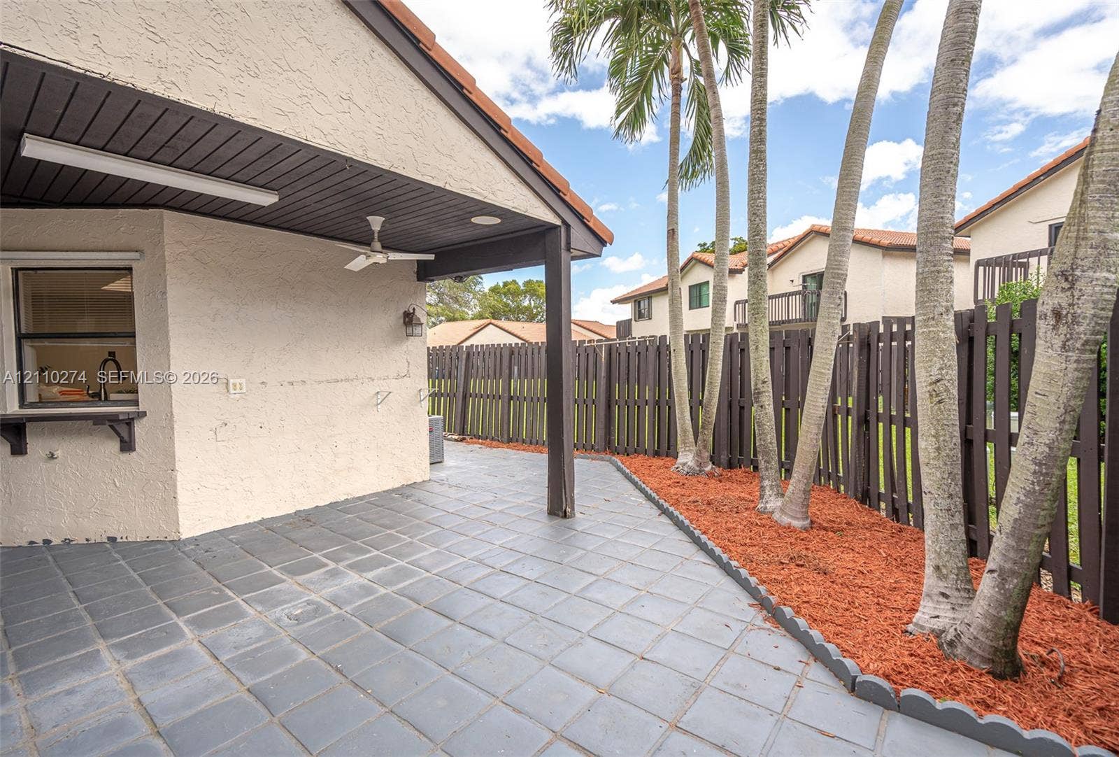14955 SW 49th Lane, #5E, Miami, FL 33185 Covered outdoor patio featuring tile flooring, a built-in service window, a ceiling fan, and a wood-slat perimeter fence