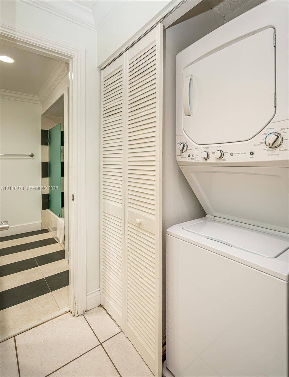 14955 SW 49th Lane, #5E, Miami, FL 33185 Laundry area featuring a stacked washer and dryer unit, white louvered bifold closet doors, and large-format tile flooring with a black and white striped pattern