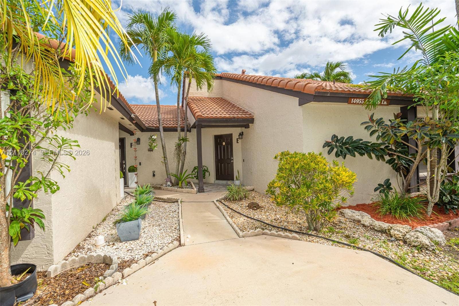 14955 SW 49th Lane, #5E, Miami, FL 33185 Stucco exterior featuring a clay tile roof, covered entryway, and xeriscaped front grounds with mature palm trees