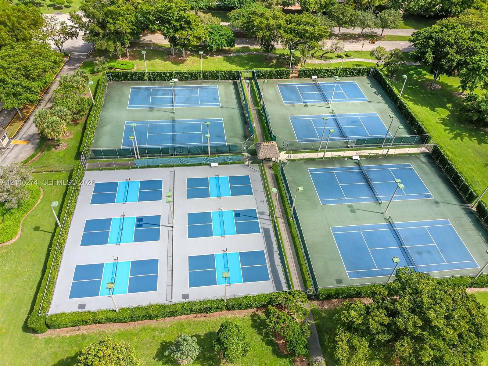 14955 SW 49th Lane, #5E, Miami, FL 33185 Outdoor recreation area featuring two dual-court tennis facilities, two multi-court pickleball setups, perimeter fencing, and manicured landscaping