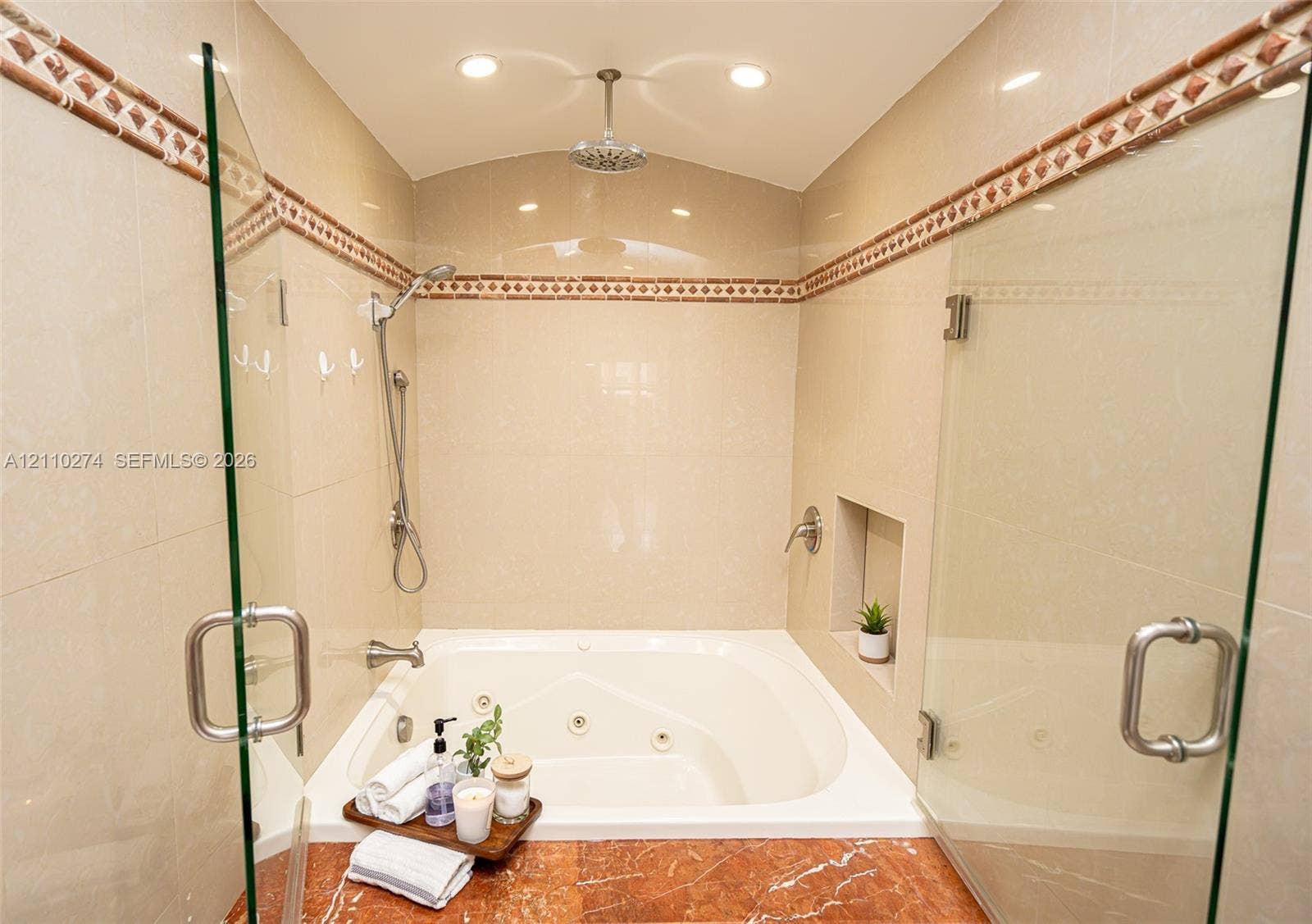14955 SW 49th Lane, #5E, Miami, FL 33185 Jetted soaking tub featuring a stone-surround deck, ceiling-mounted rainfall shower head, handheld sprayer, glass enclosure, and decorative tile inlay