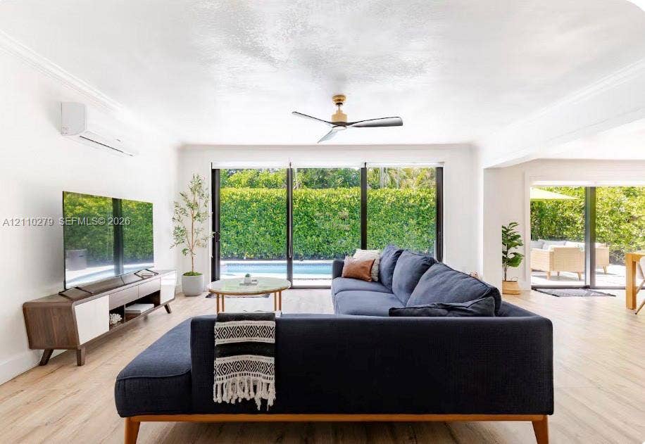 Living area featuring wood-finish flooring, floor-to-ceiling sliding glass doors, wall-mounted ductless air conditioning unit, and a ceiling fan
