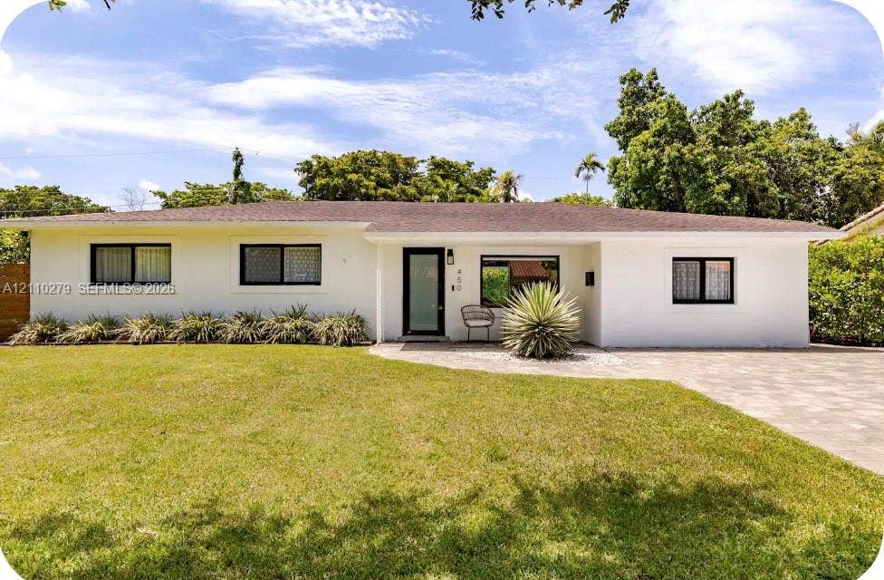 Single-story exterior featuring white stucco siding, a low-pitched roof, black-framed windows, and a paver driveway