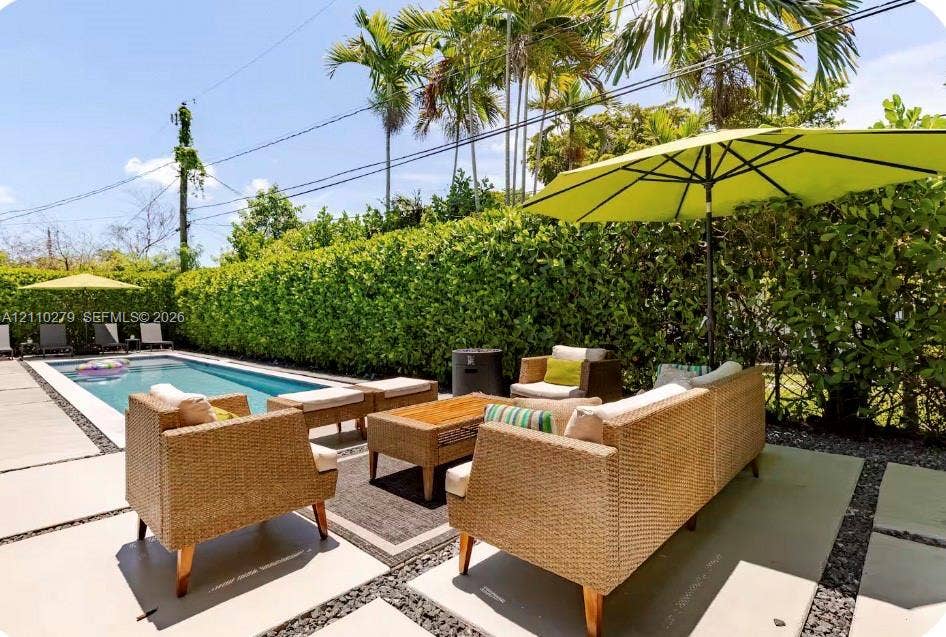 Covered patio featuring a woven reed pergola, concrete paver decking, stone aggregate inlay, and a rectangular swimming pool surrounded by a manicured hedge