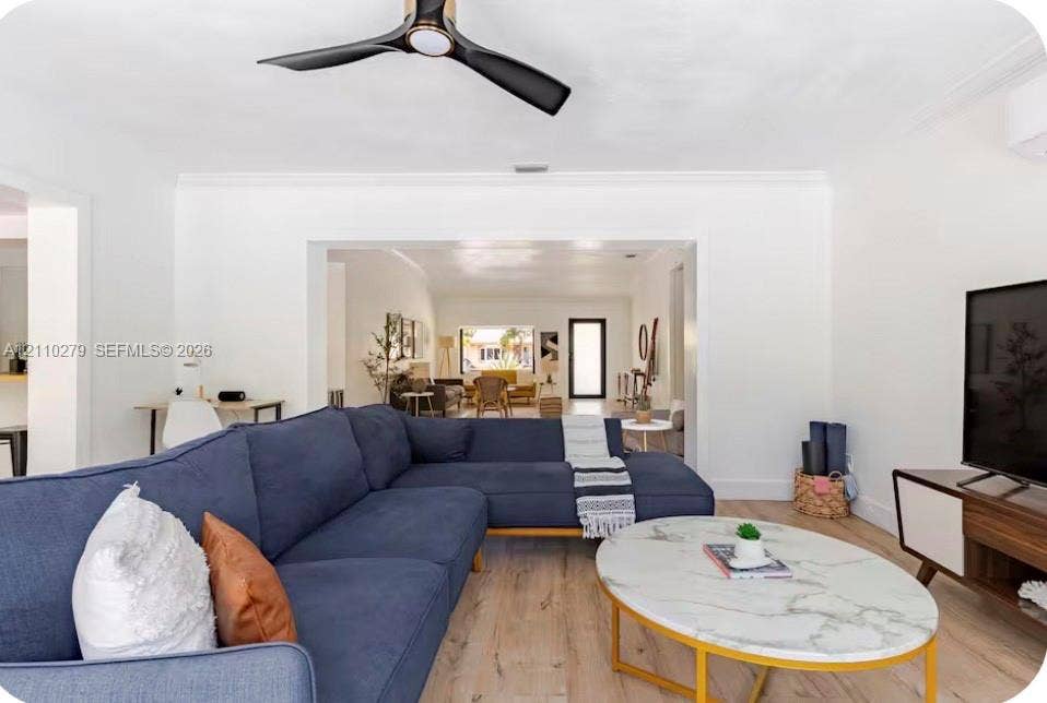 Open-concept interior featuring light wood-finish flooring, a contemporary three-blade ceiling fan, crown molding, and a wall-mounted ductless climate control unit