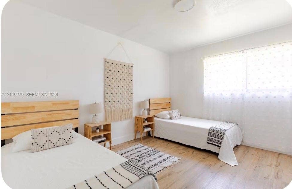 Neutral-toned interior space featuring wood-finish flooring, white walls, and a large window with natural light