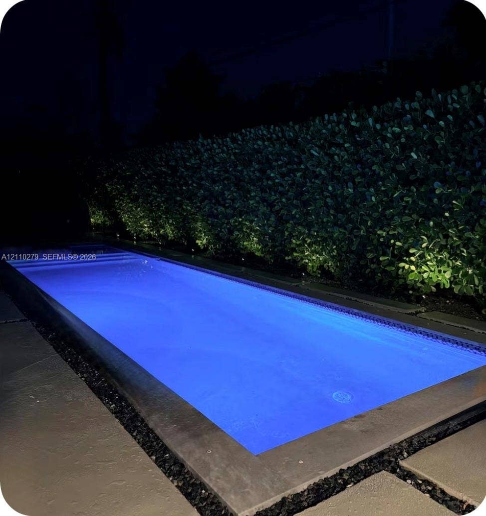Rectangular pool with submerged stairs, bordered by large-format concrete pavers, decorative stone aggregate, and a manicured hedge