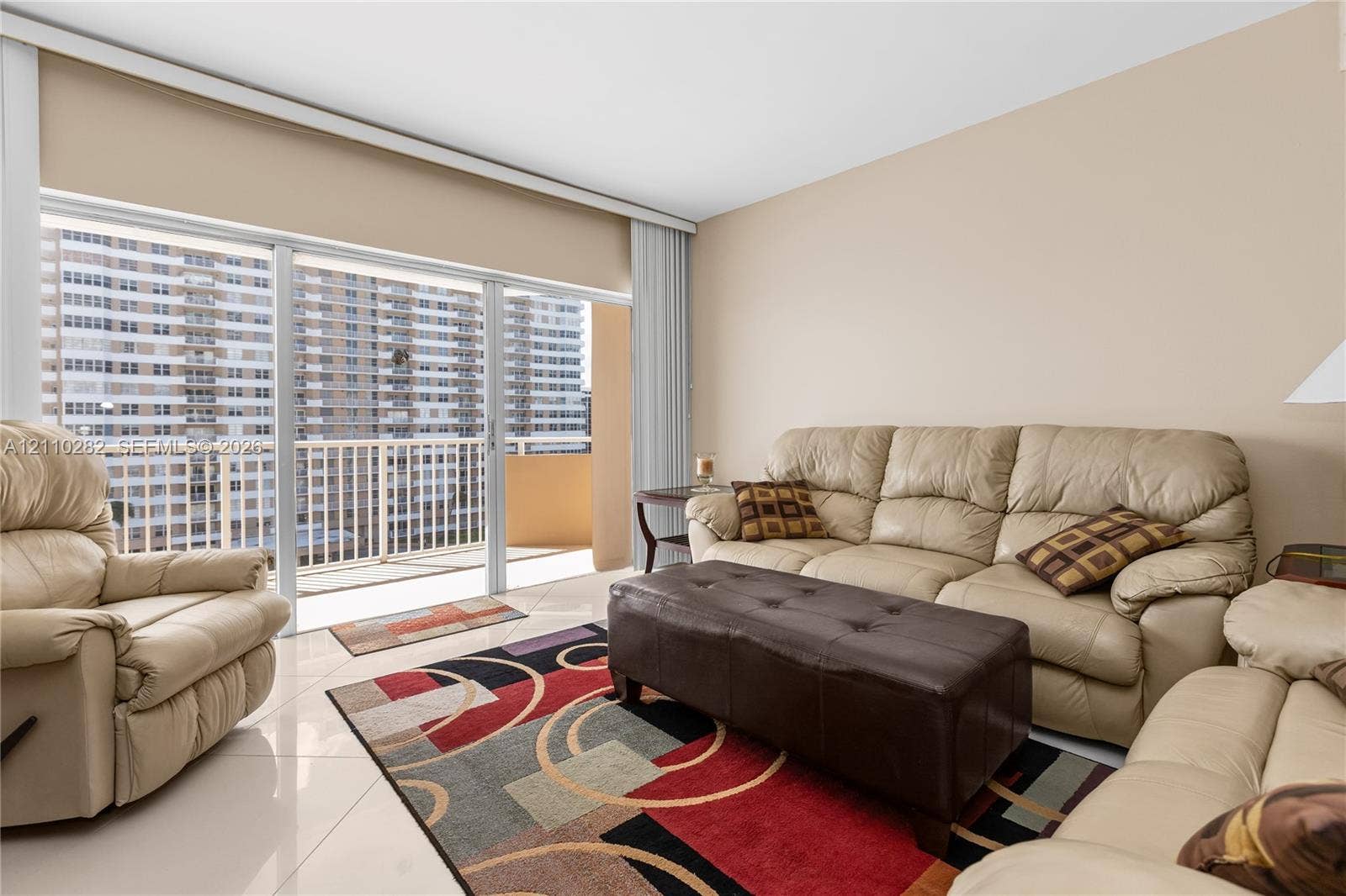 Floor-to-ceiling sliding glass doors with access to an exterior balcony, light-colored tile flooring, and vertical blinds