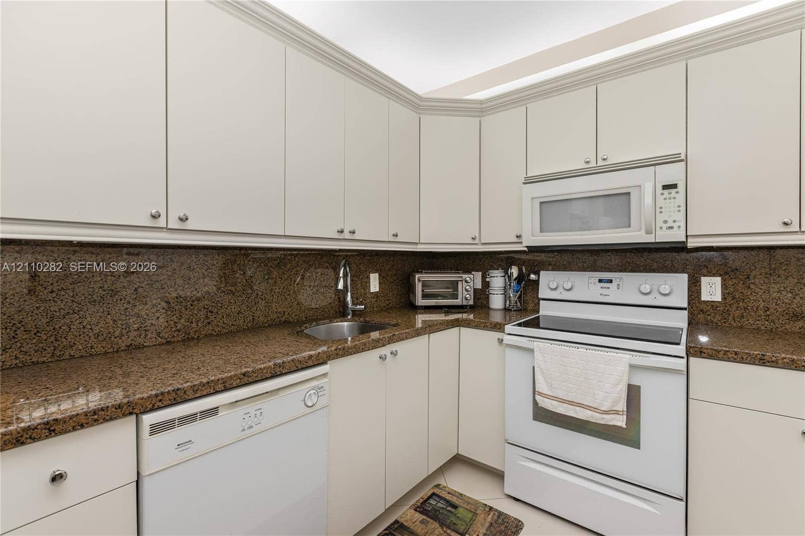 Kitchen featuring white cabinetry, stone-finish countertops, an undermount sink, and integrated white appliances