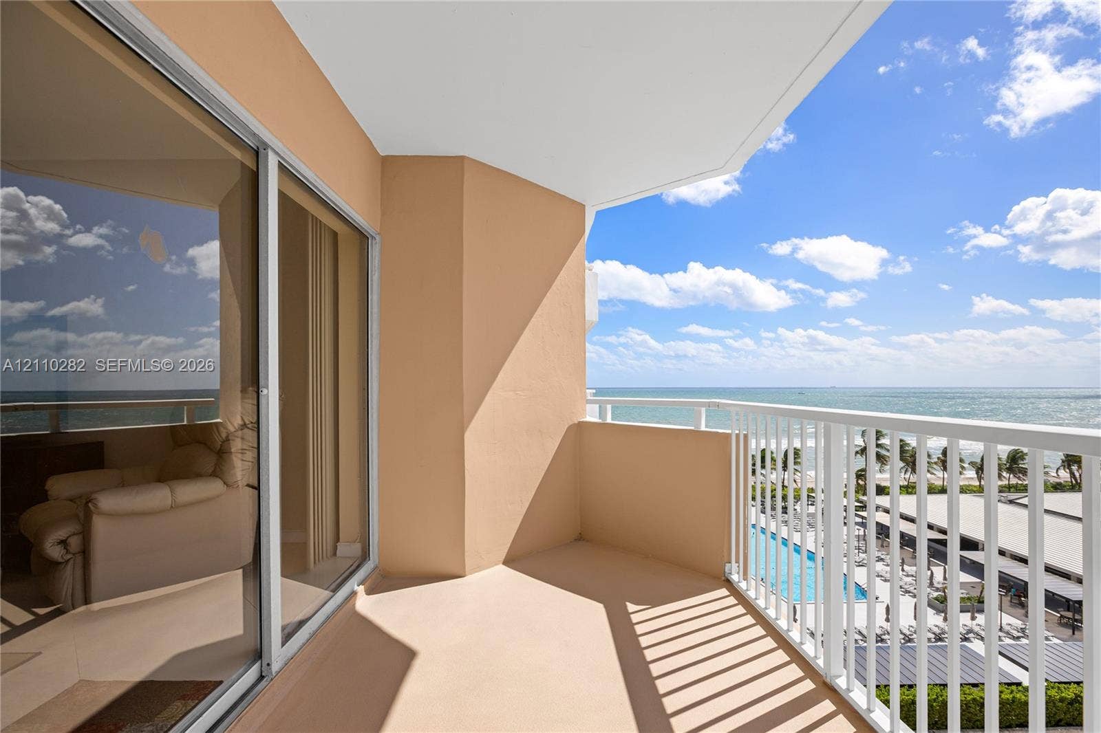 Covered balcony featuring white vertical railings, expansive glass sliding doors, and ocean frontage
