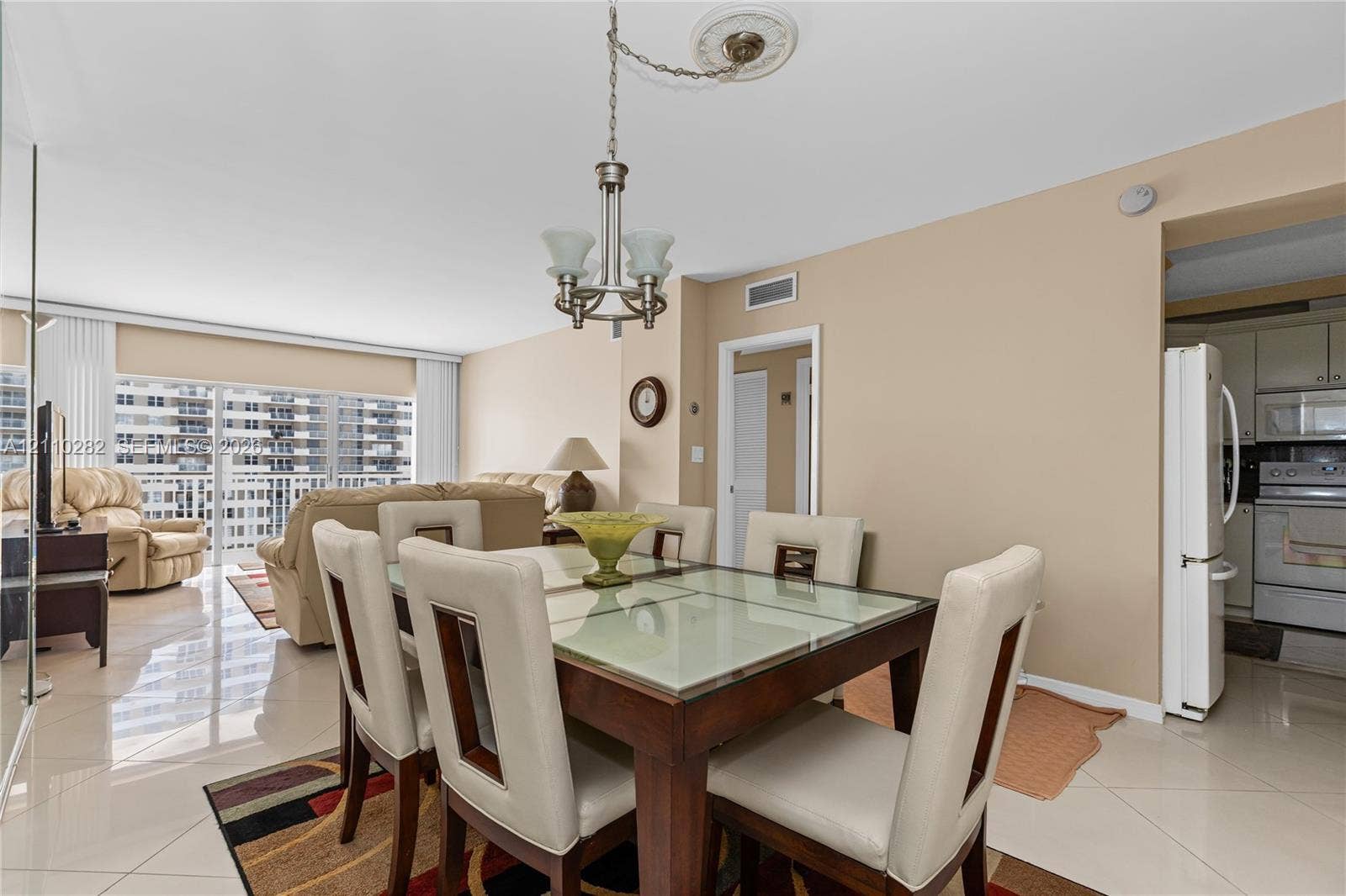 Open-concept dining area featuring polished tile flooring, a multi-light chandelier with a decorative ceiling medallion, and floor-to-ceiling glass sliding doors leading to a balcony