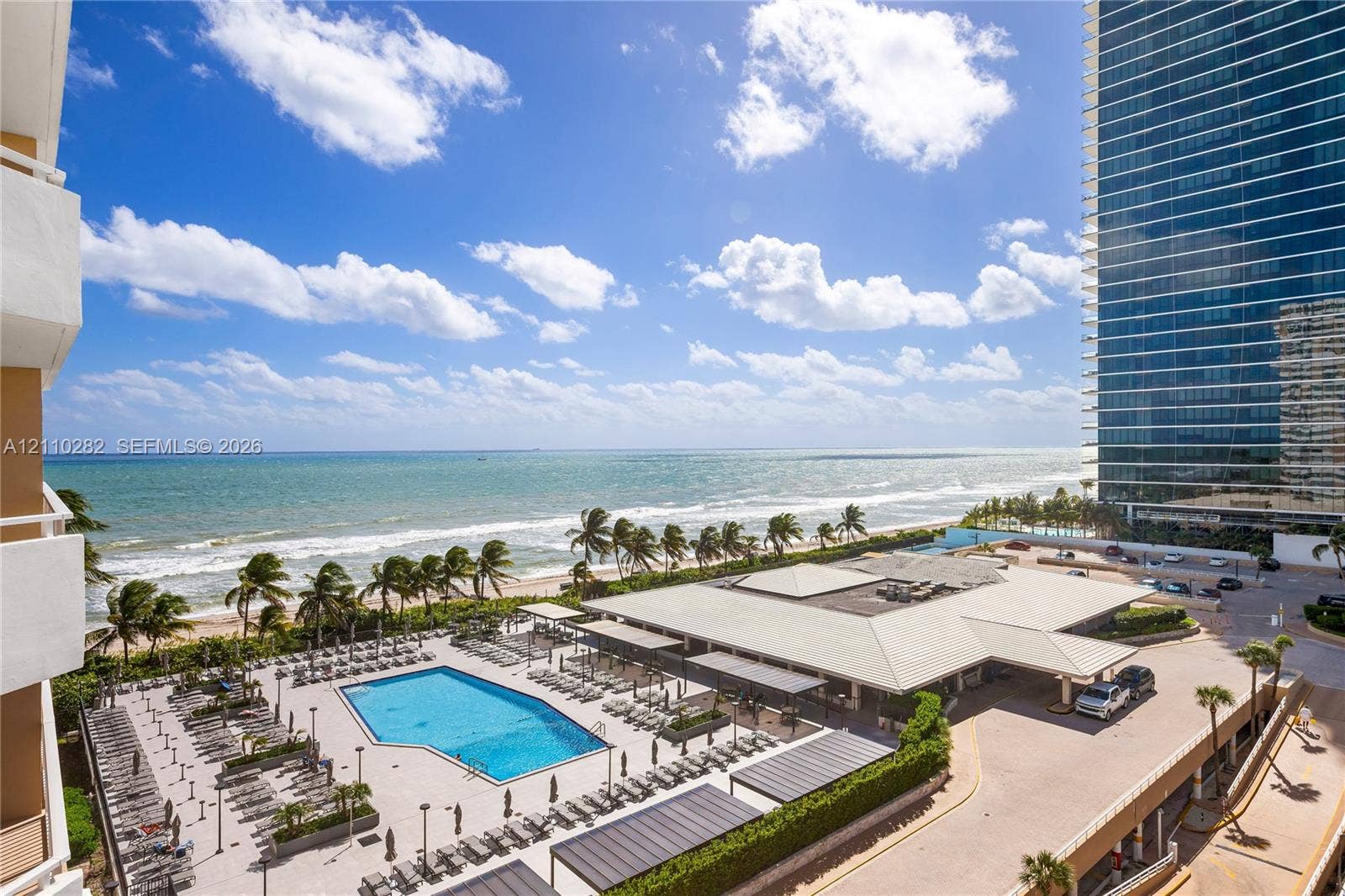 Oceanfront complex featuring a swimming pool, paved pool deck, multi-story high-rise building, and direct proximity to the beach