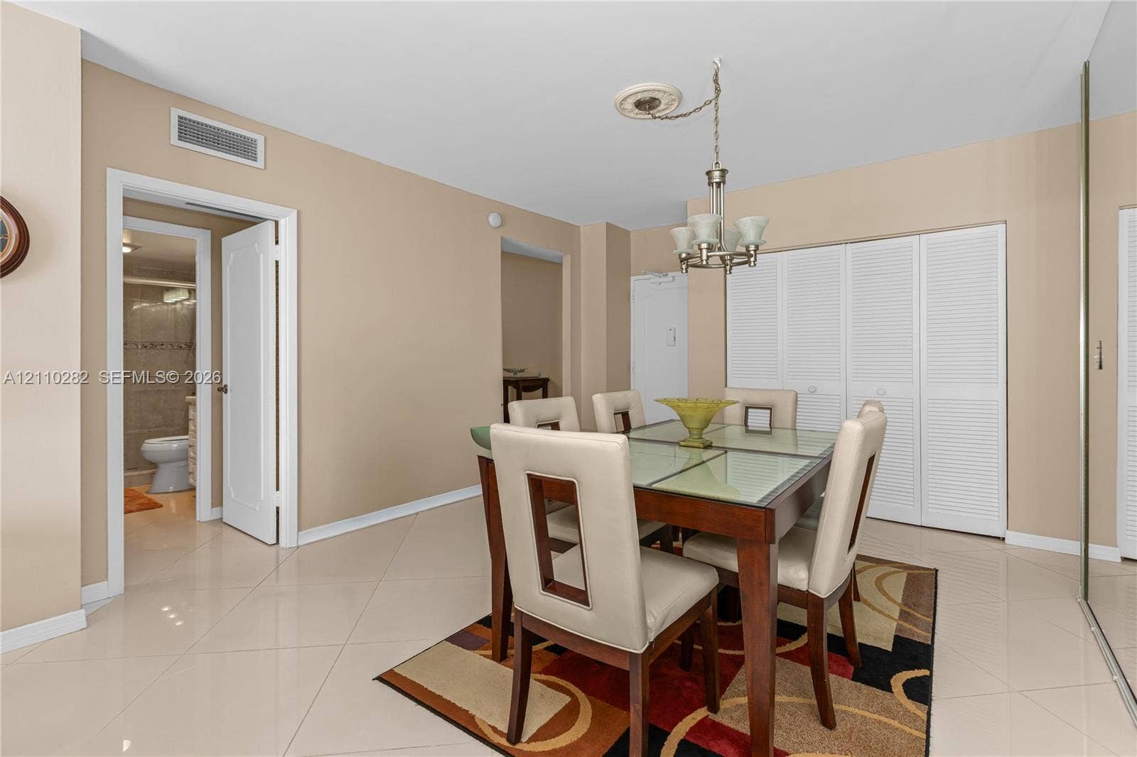 Spacious interior featuring large-format tile flooring, a multi-arm chandelier with a decorative ceiling medallion, and floor-to-ceiling white louvered closet doors